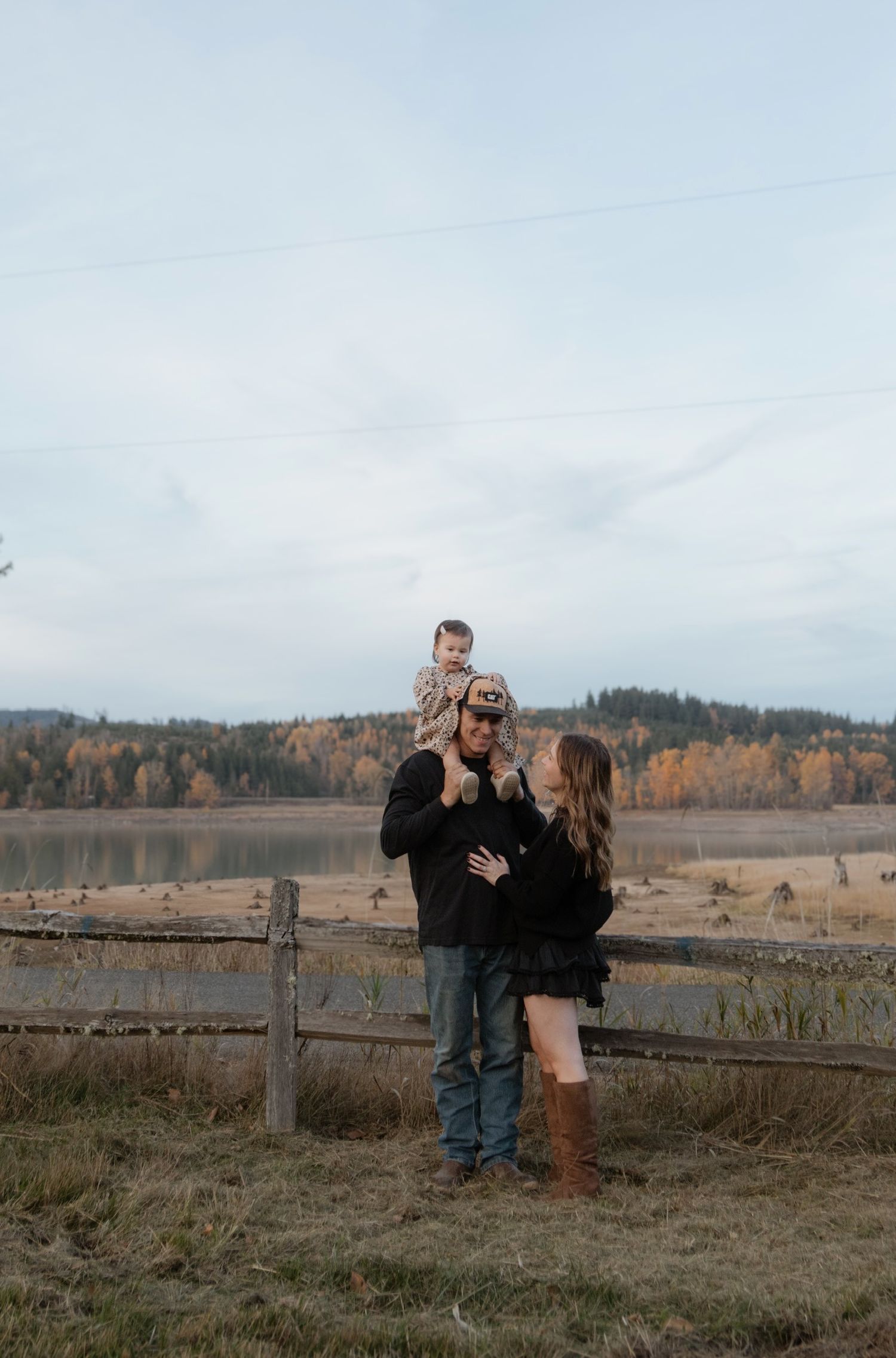 A family stands together against an autumn lake landscape with mountains in the background.