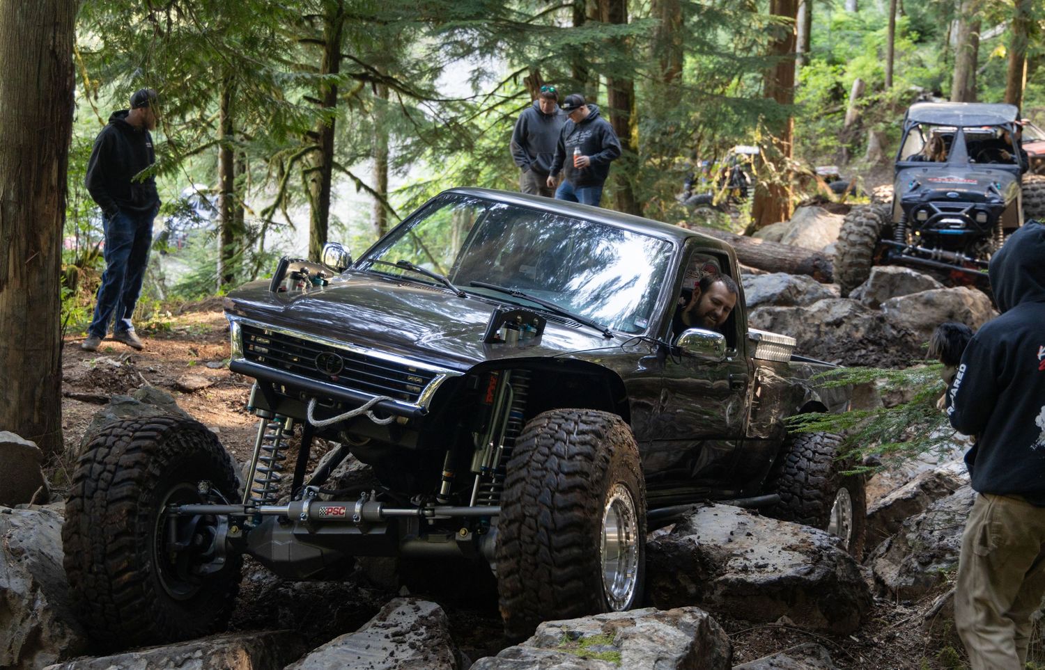 A black off-road vehicle navigates challenging rocky terrain on a forest trail during an outdoor adventure expedition.