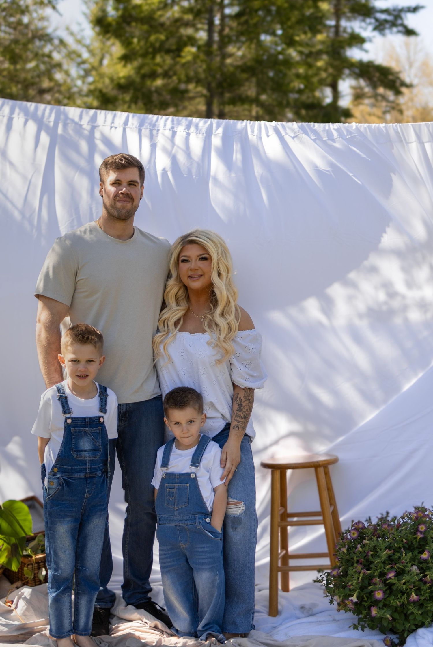 A family wearing matching denim outfits poses together against a white backdrop in an outdoor photo session.