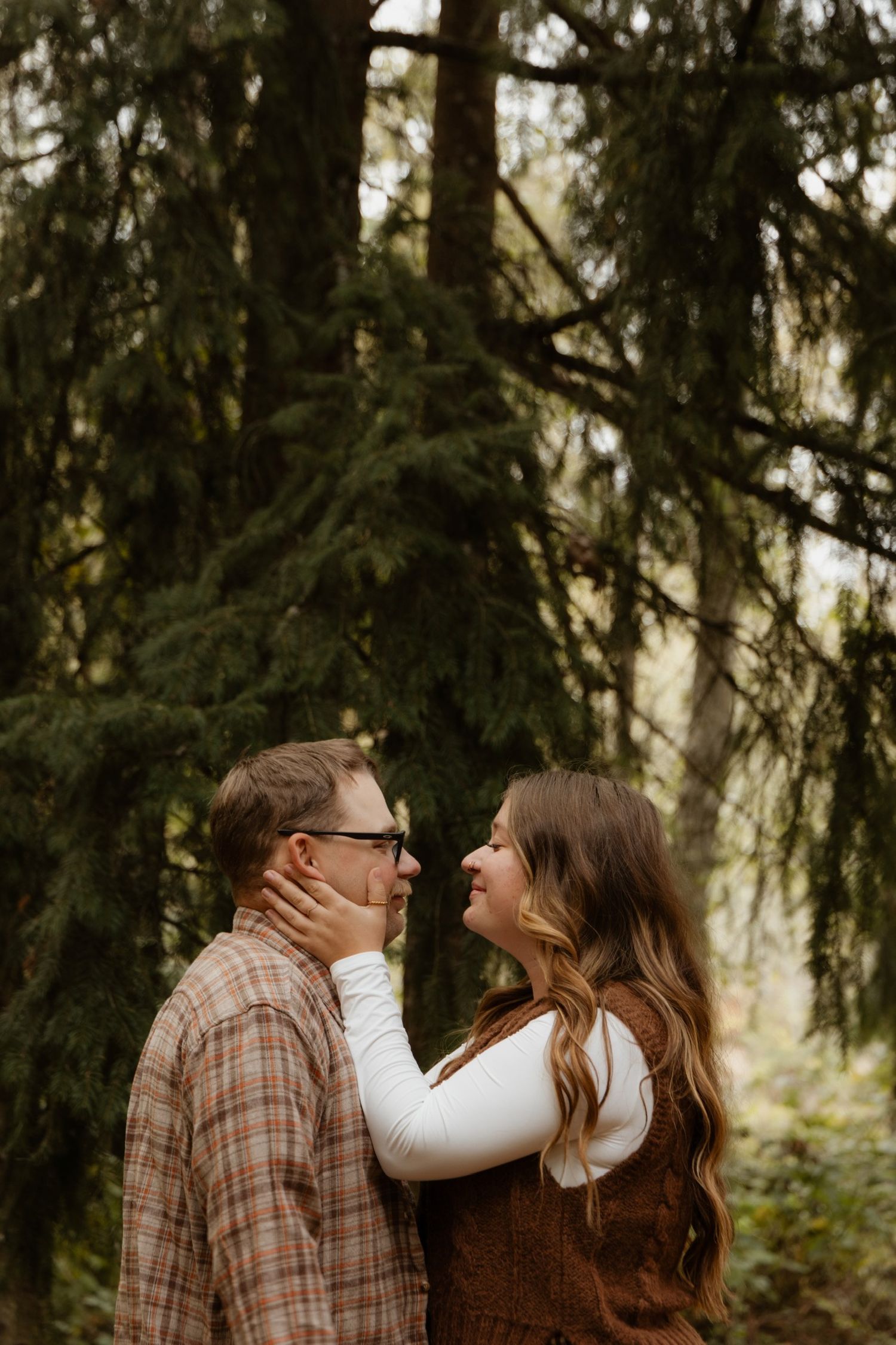 A couple shares intimate moments in a wooded forest setting during autumn.