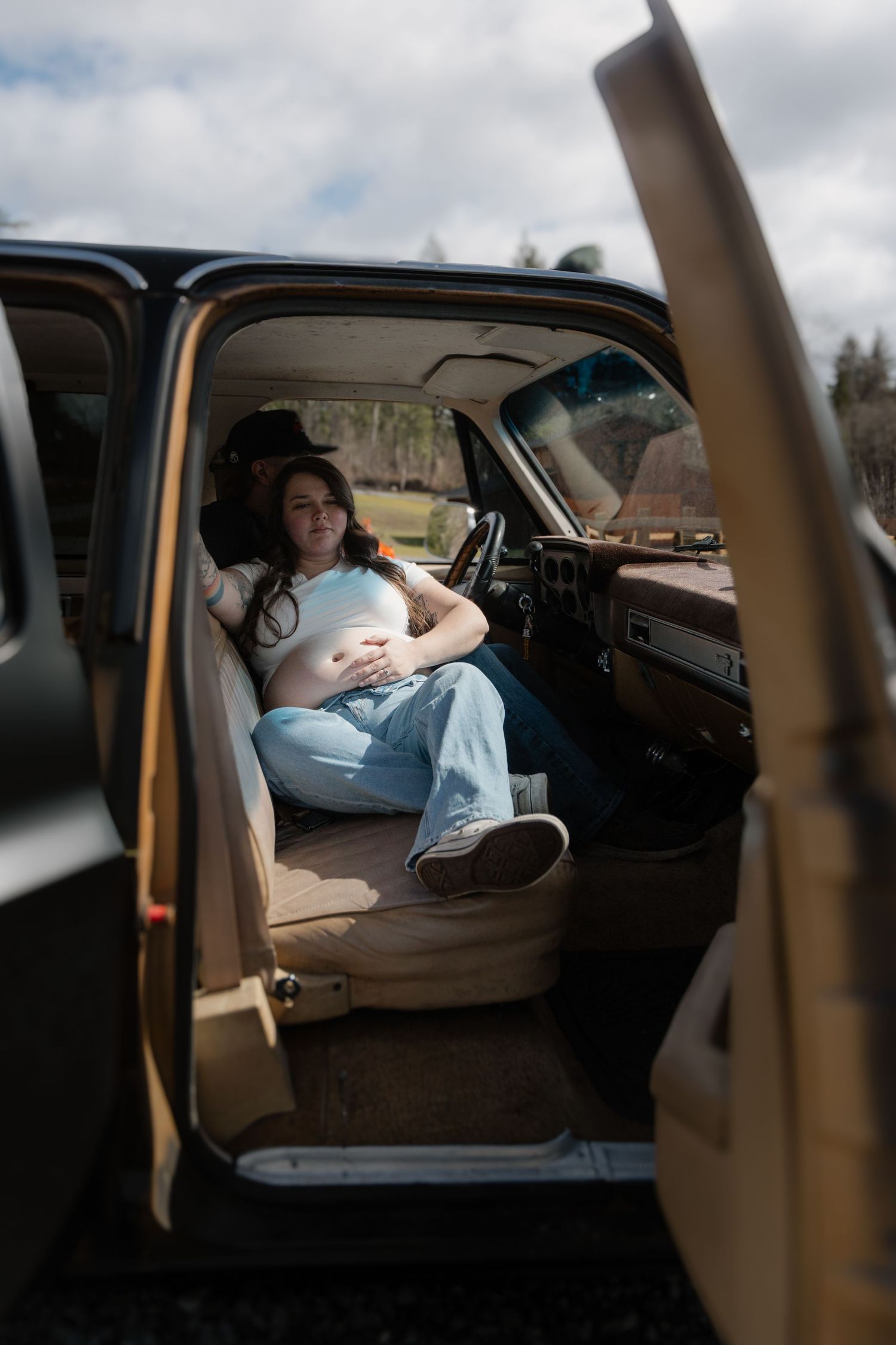 View through open car door of someone relaxing in vintage vehicle with brown interior on cloudy day.
