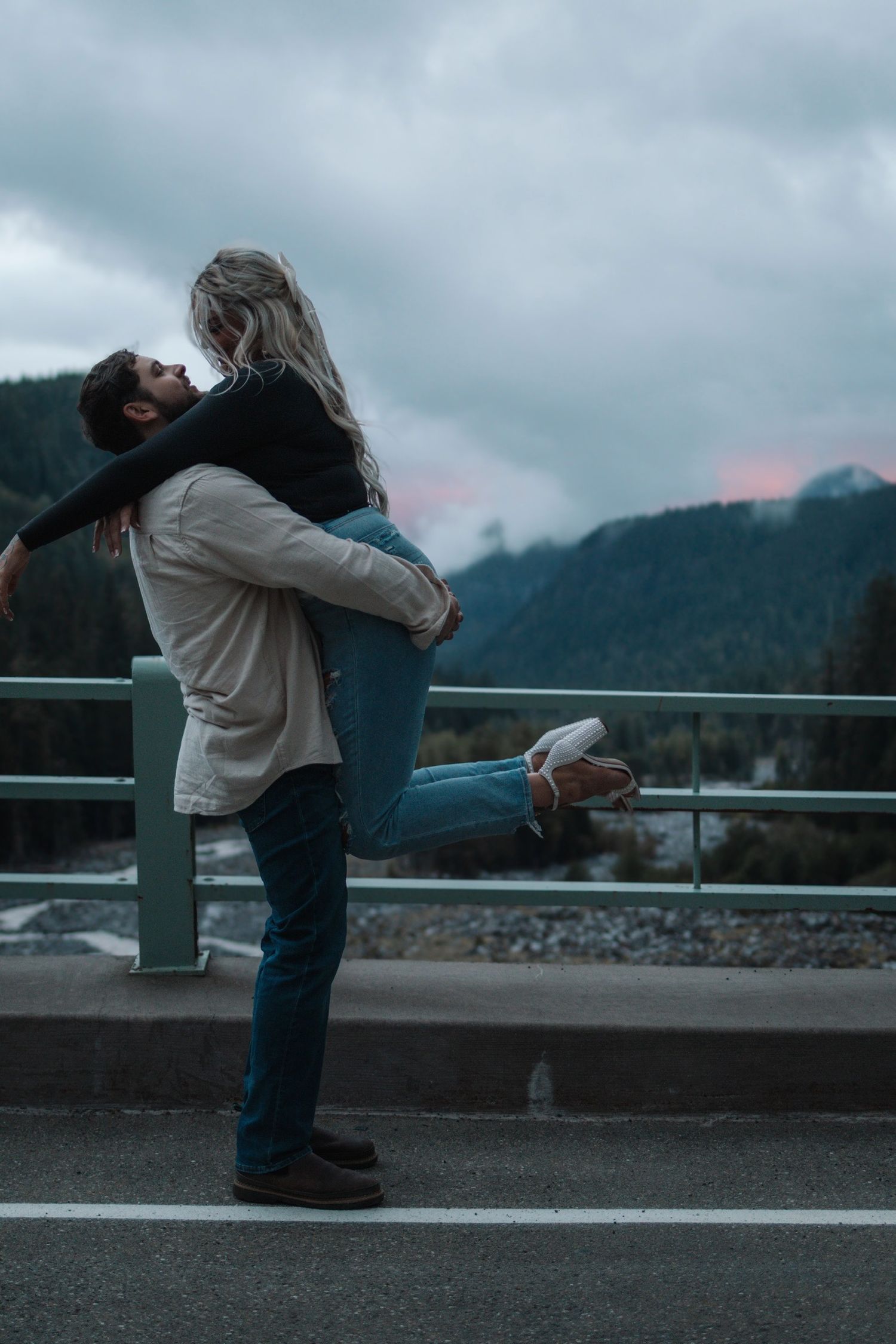 A romantic embrace captured against a misty mountain backdrop on a cloudy day.