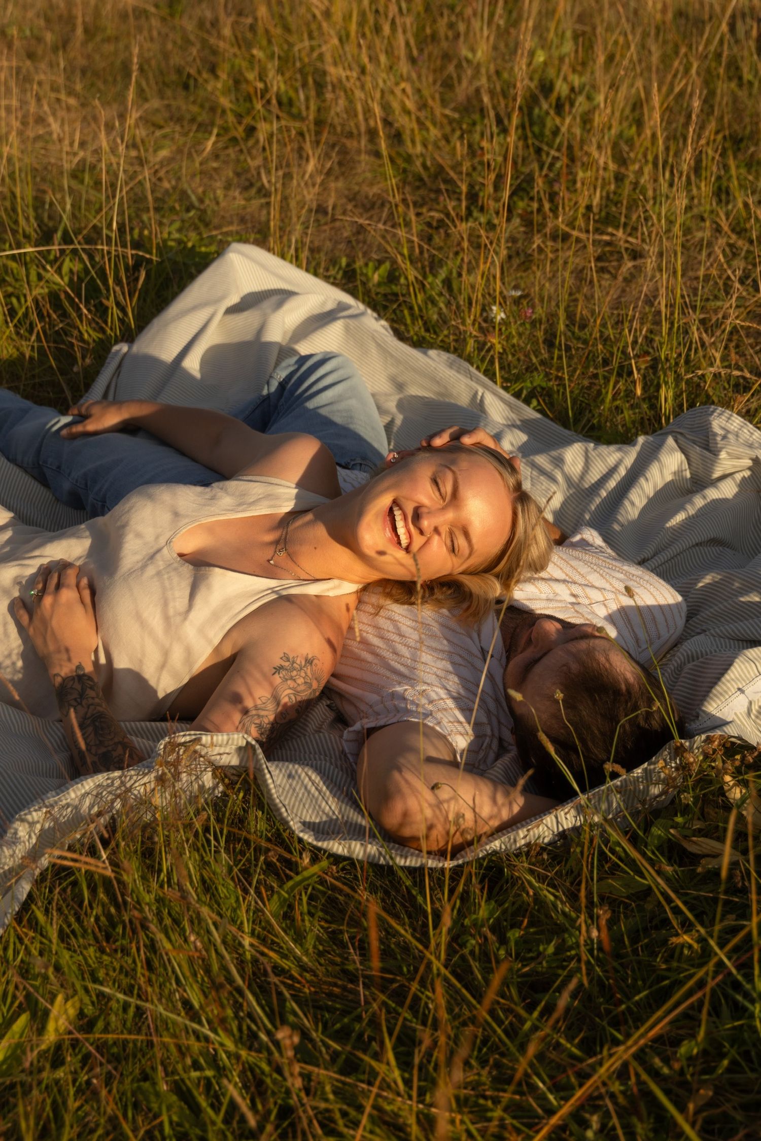 A couple relaxing on a white blanket in a sun-drenched meadow during golden hour.