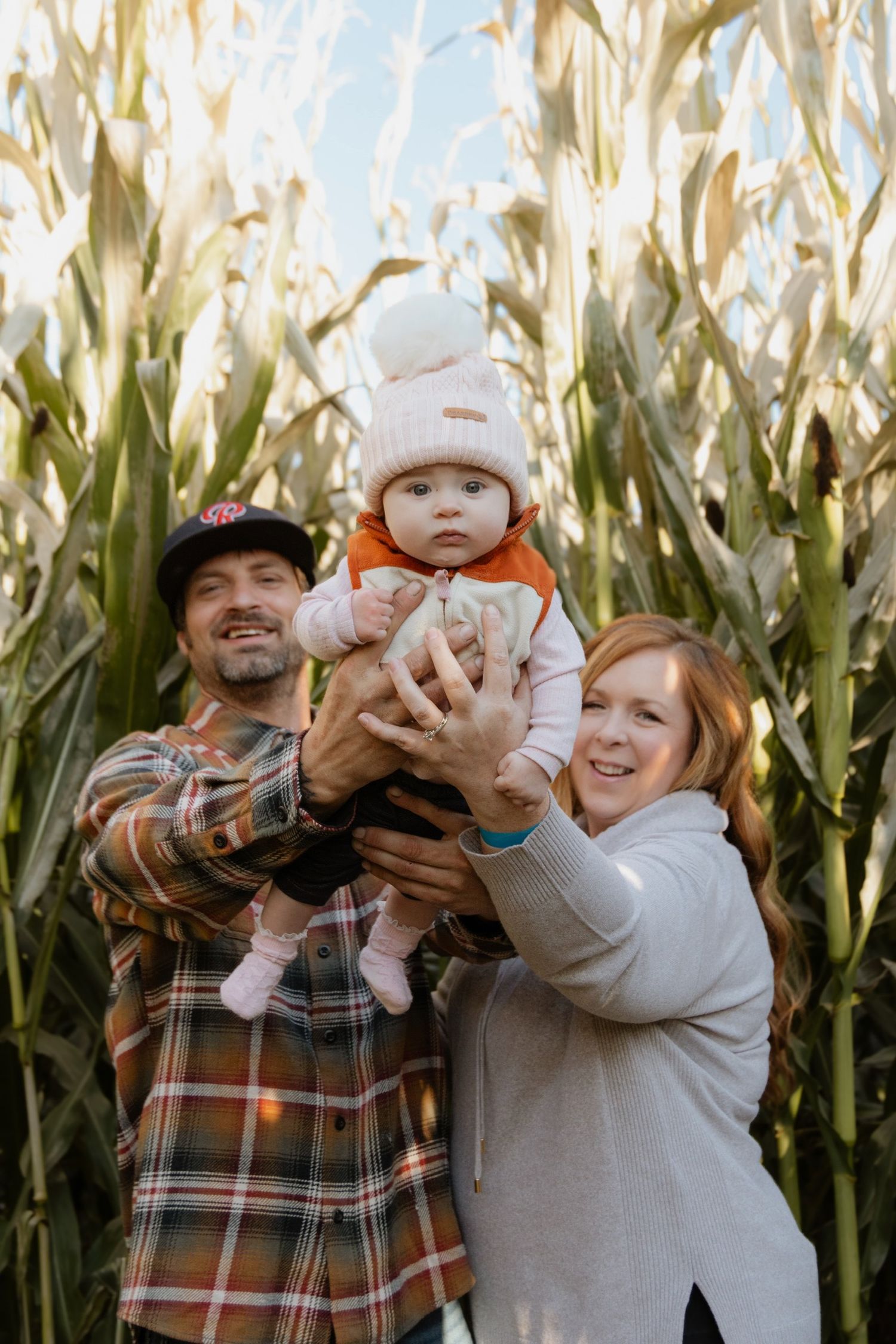 A family poses playfully in front of tall corn stalks during a fall photo session.