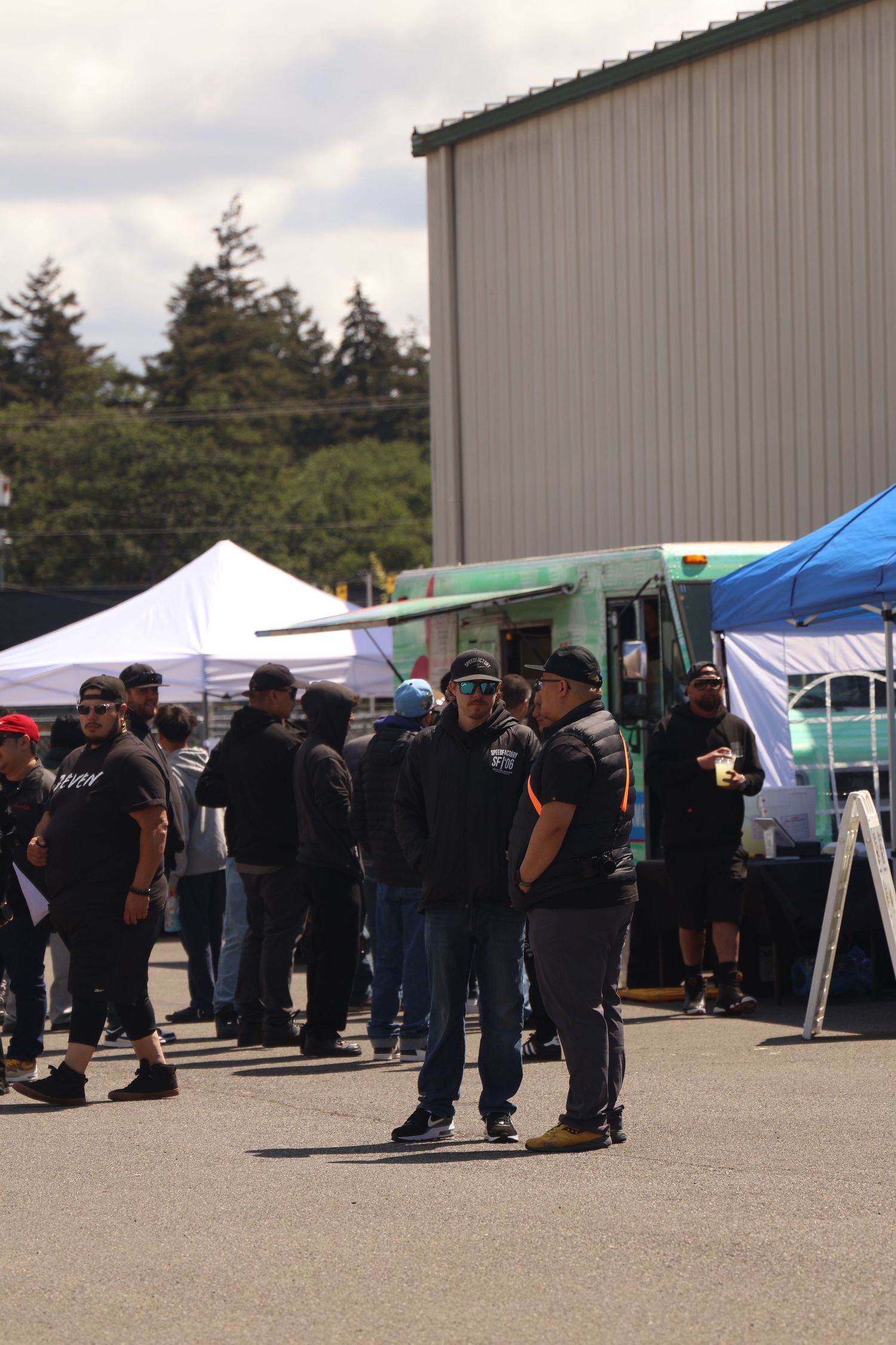 A long line of people waiting outdoors near beige buildings and tents at a community event or gathering.