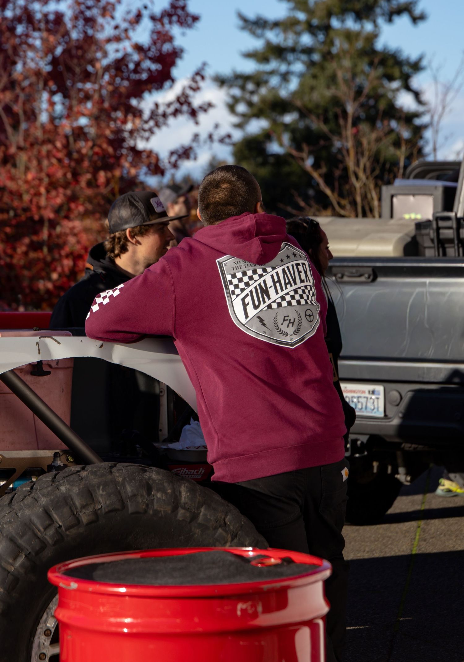 Burgundy apparel with racing logos displayed near vehicles and red equipment outdoors.