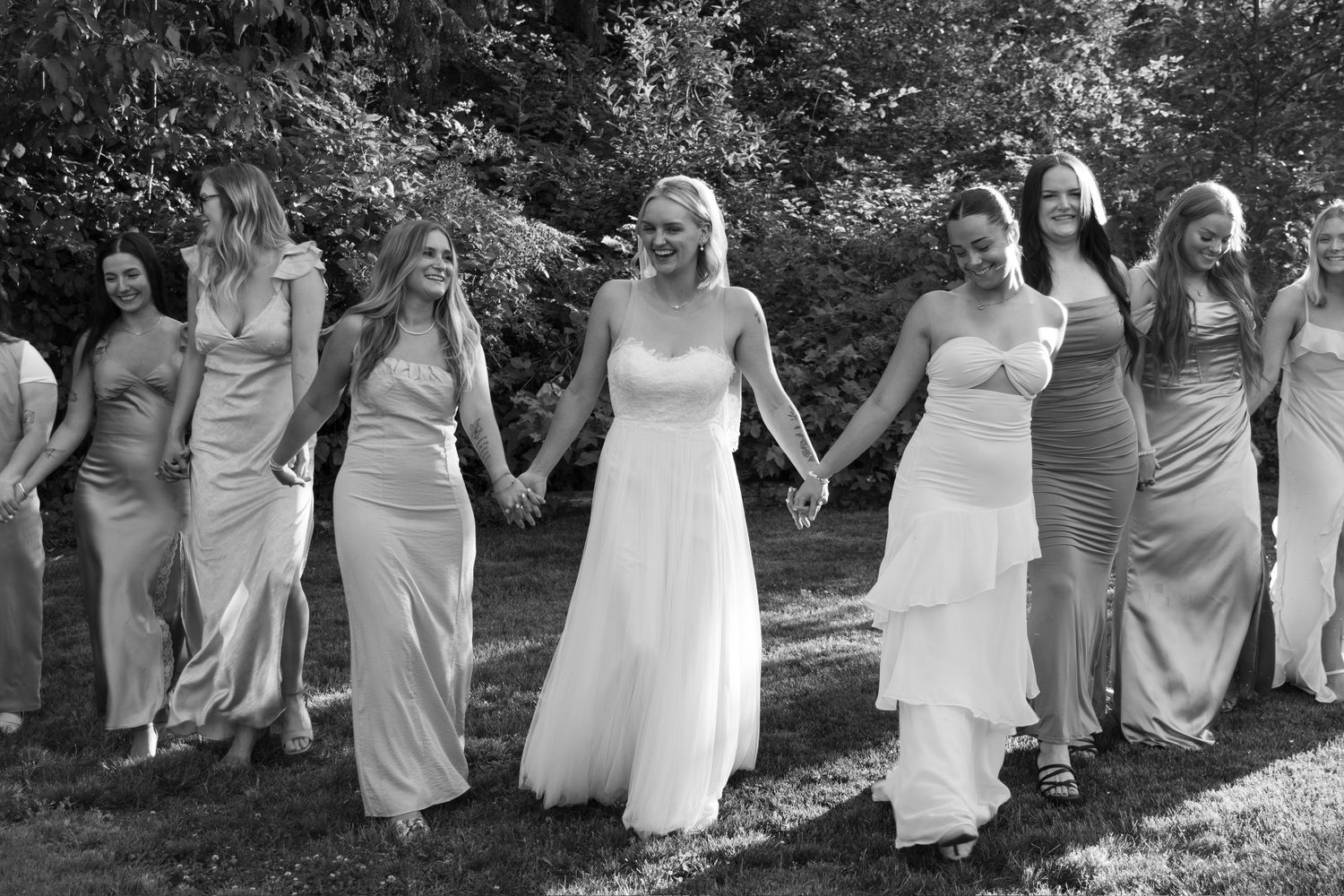 Wedding party members lined up in elegant dresses for a group photo outdoors.