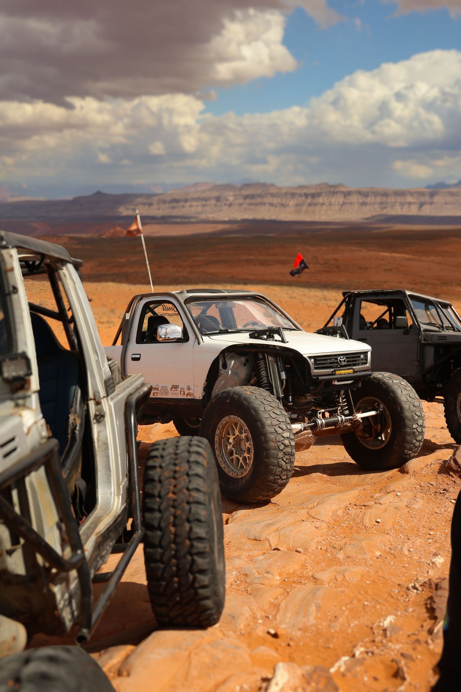 Off-road vehicles lined up against dramatic desert landscape with cloudy skies.
