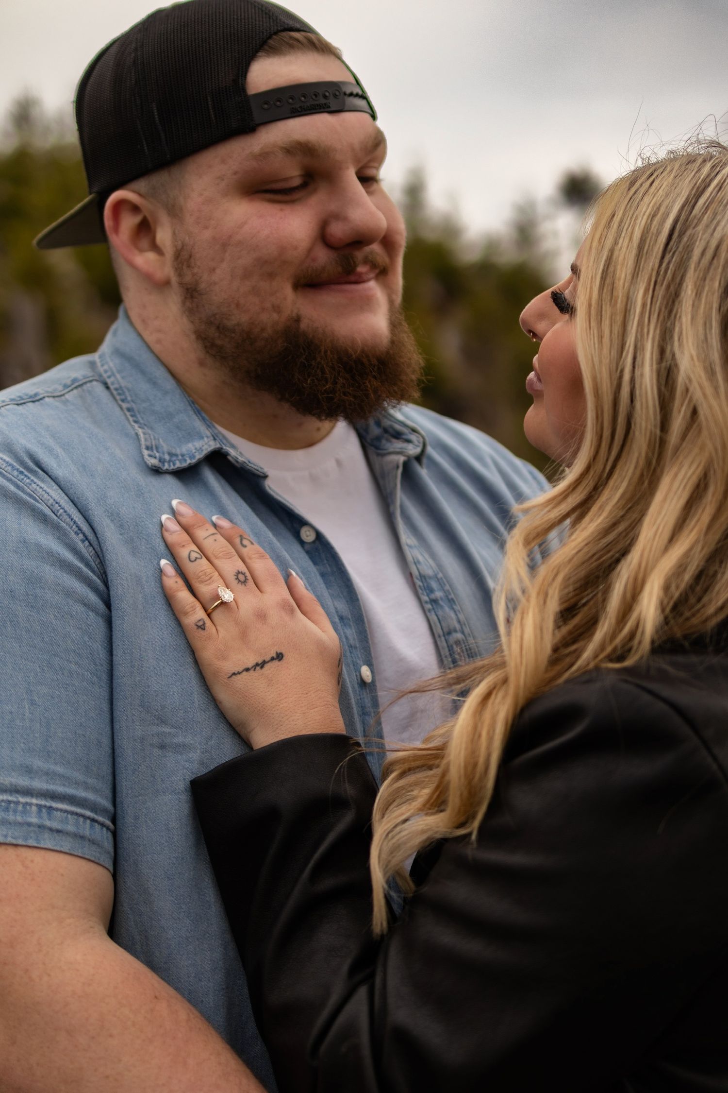 A couple shares an intimate moment outdoors, with the person in denim embracing their partner wearing black.