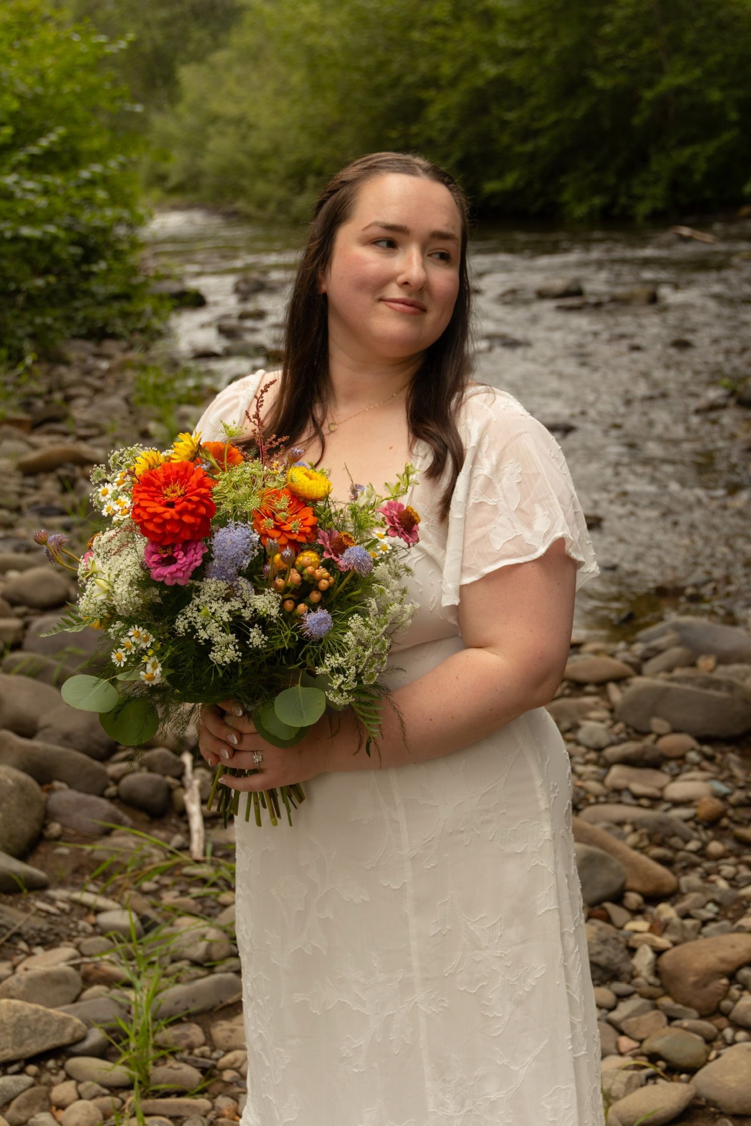 A beautiful bridal portrait with vibrant wildflower bouquet by a rocky stream.