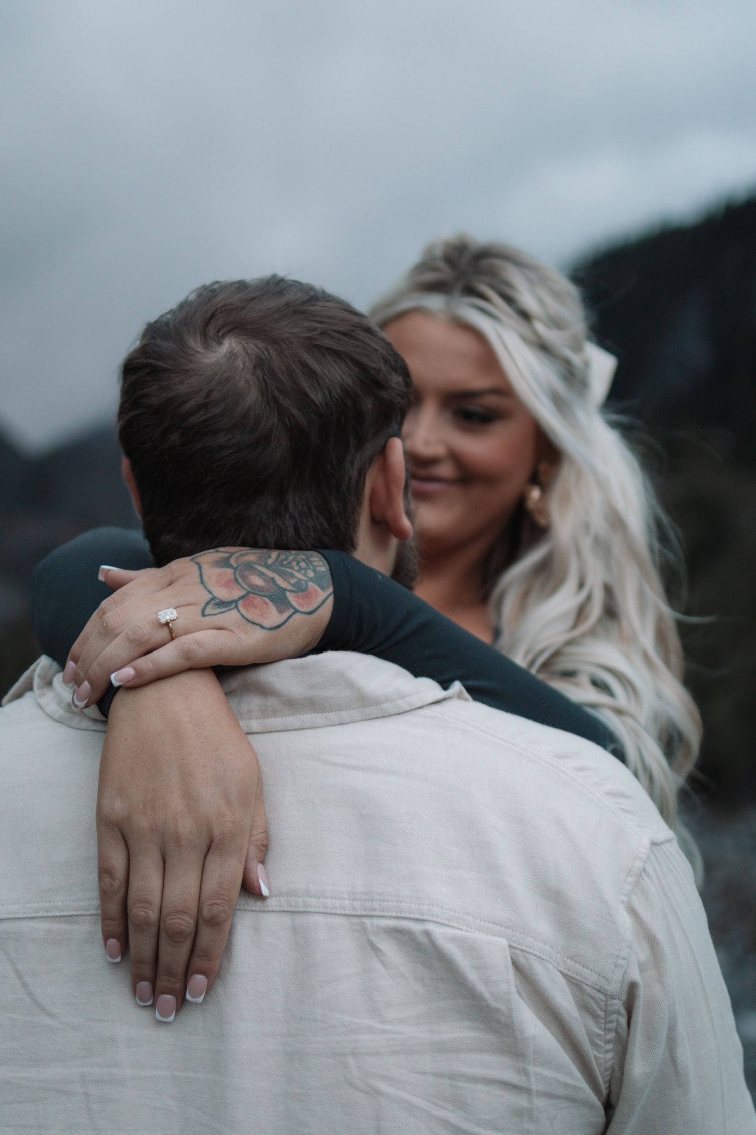 Close-up shot showing hands embracing with a visible tattoo against a light background.