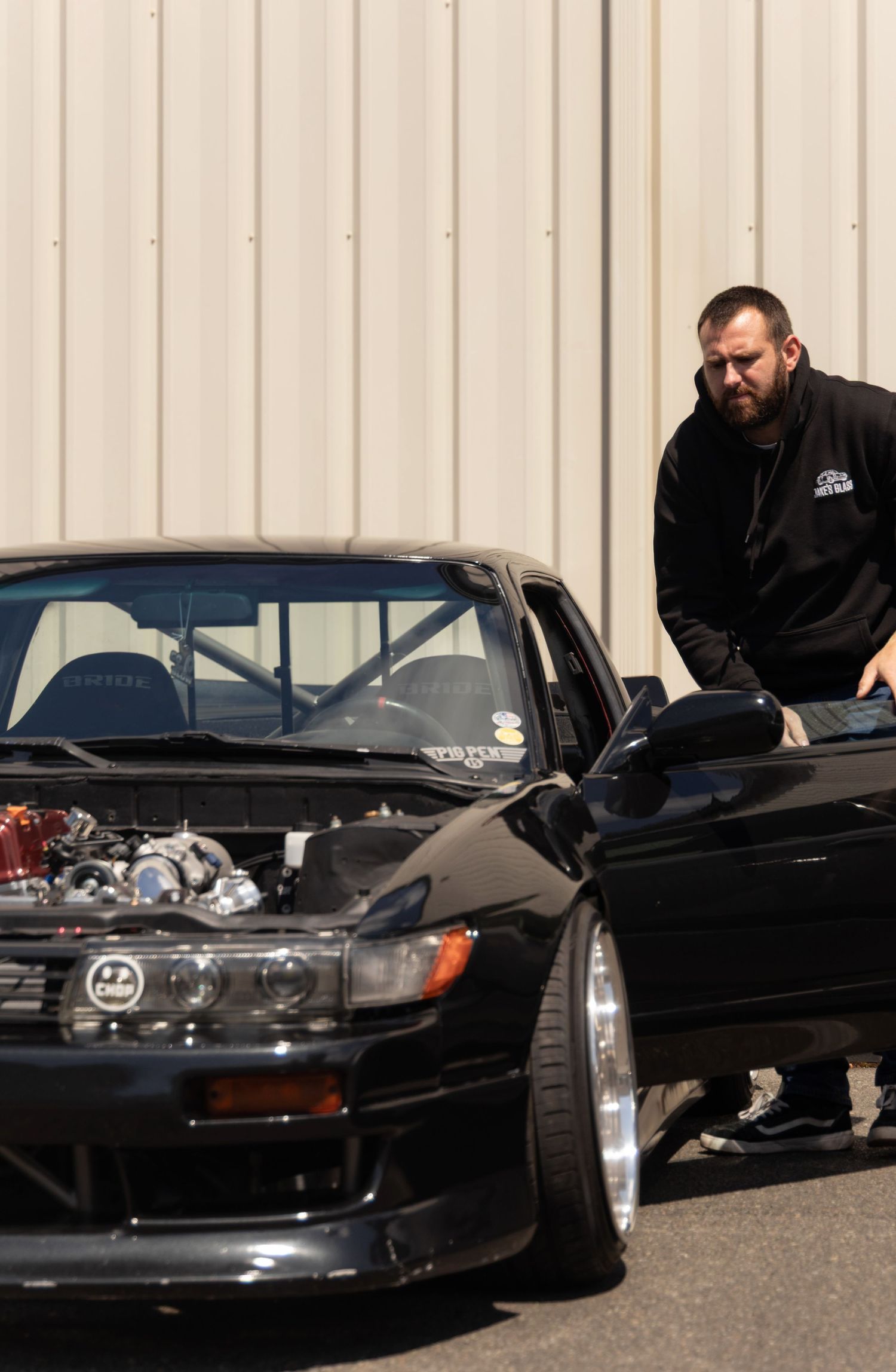Multiple black sports cars lined up in a row with a person inspecting the engine bay of one vehicle.