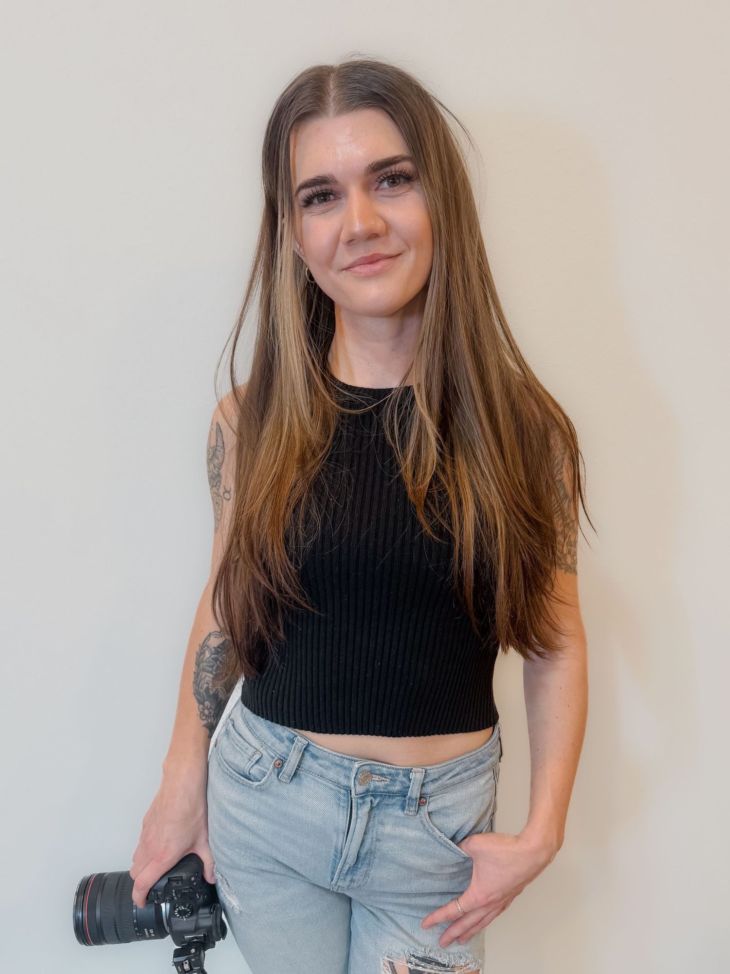Person in black crop top and light wash jeans poses against white wall in casual fashion photo series.