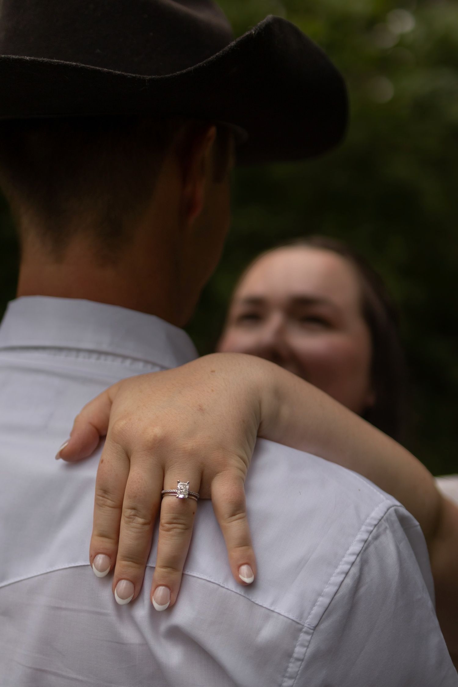 Close-up view of hands wearing an engagement ring against a white shirt background.