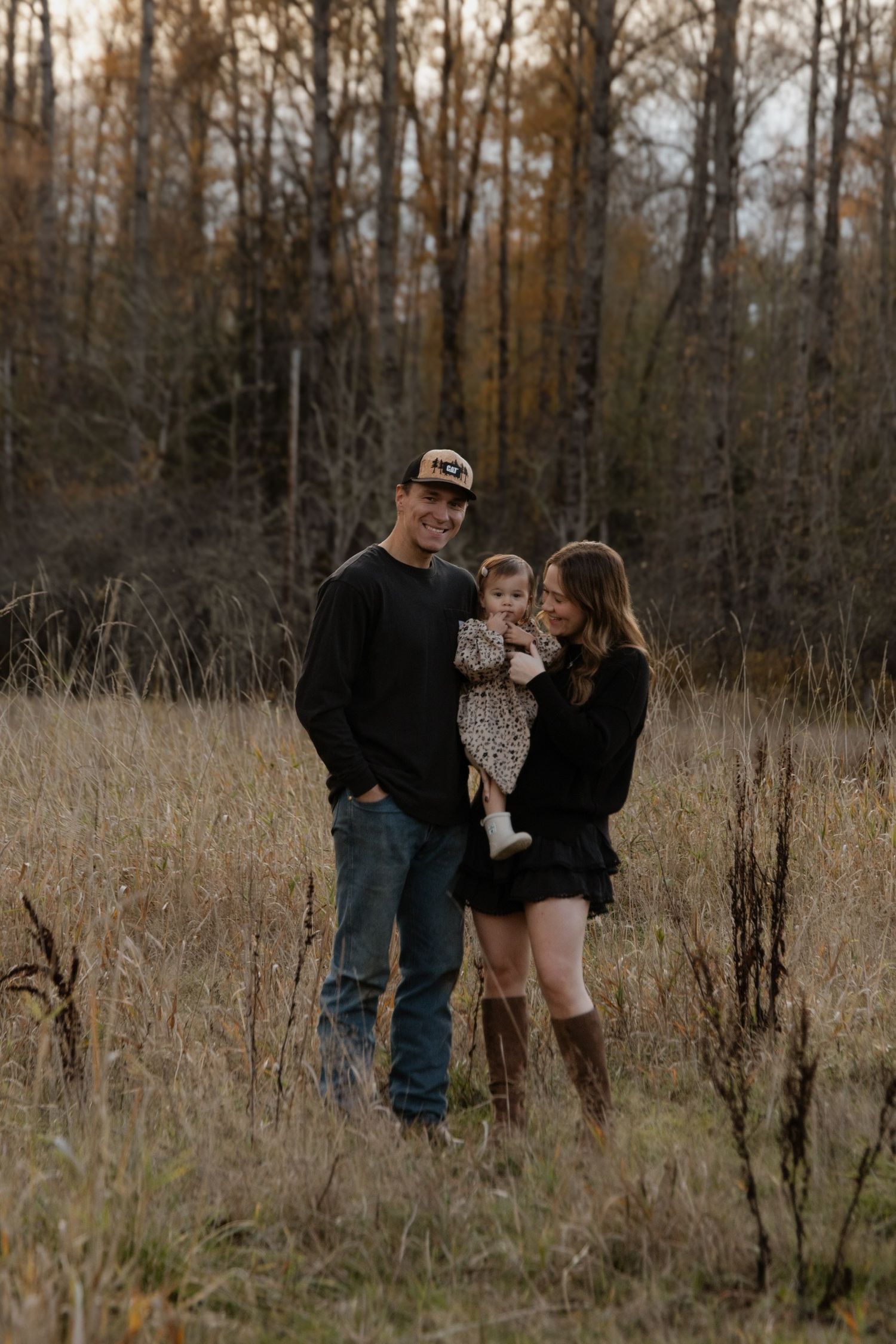 A family portrait in tall autumn grass with forest trees in the background.
