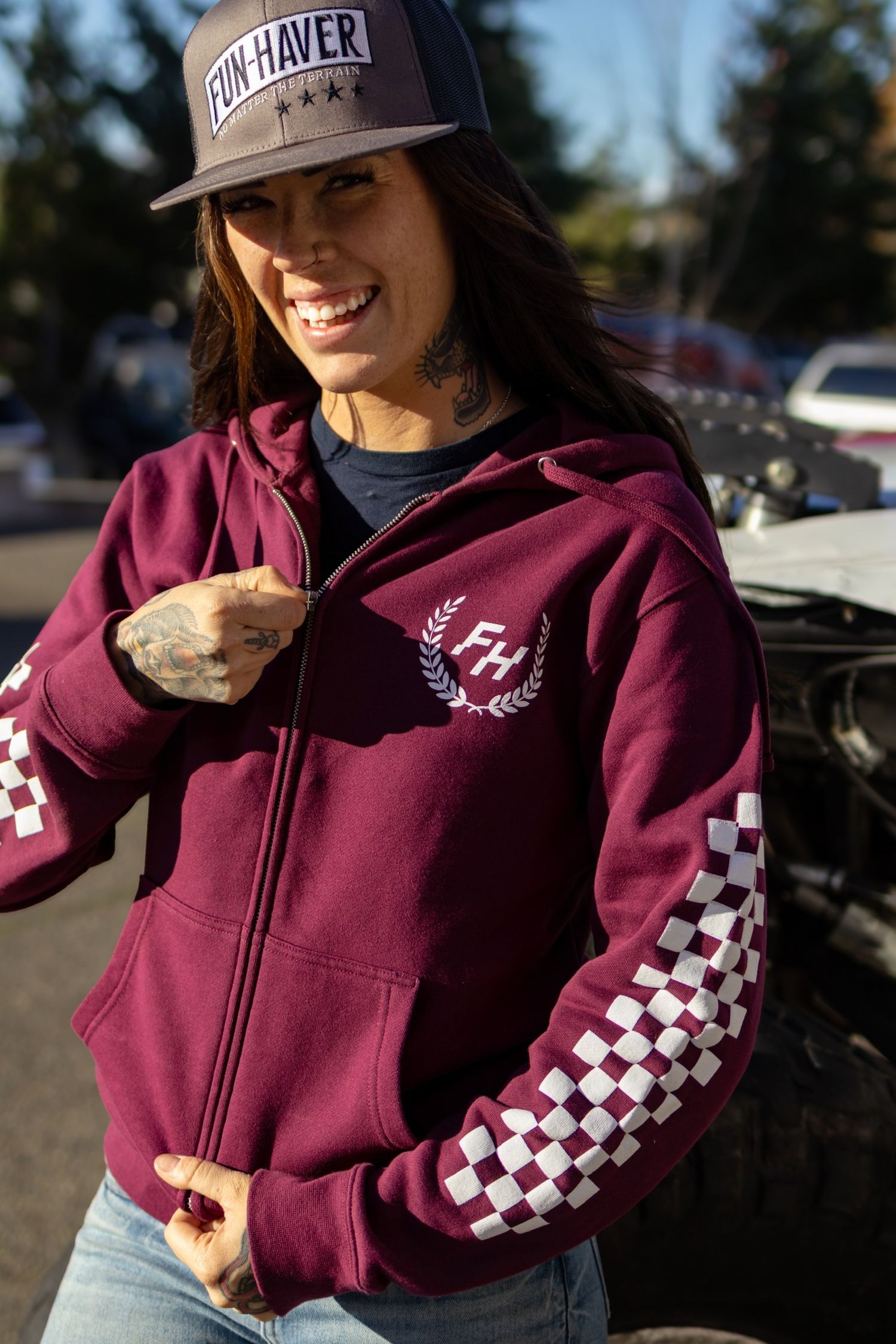Person wearing a maroon zip-up hoodie with checkered sleeve pattern and baseball cap in outdoor setting.