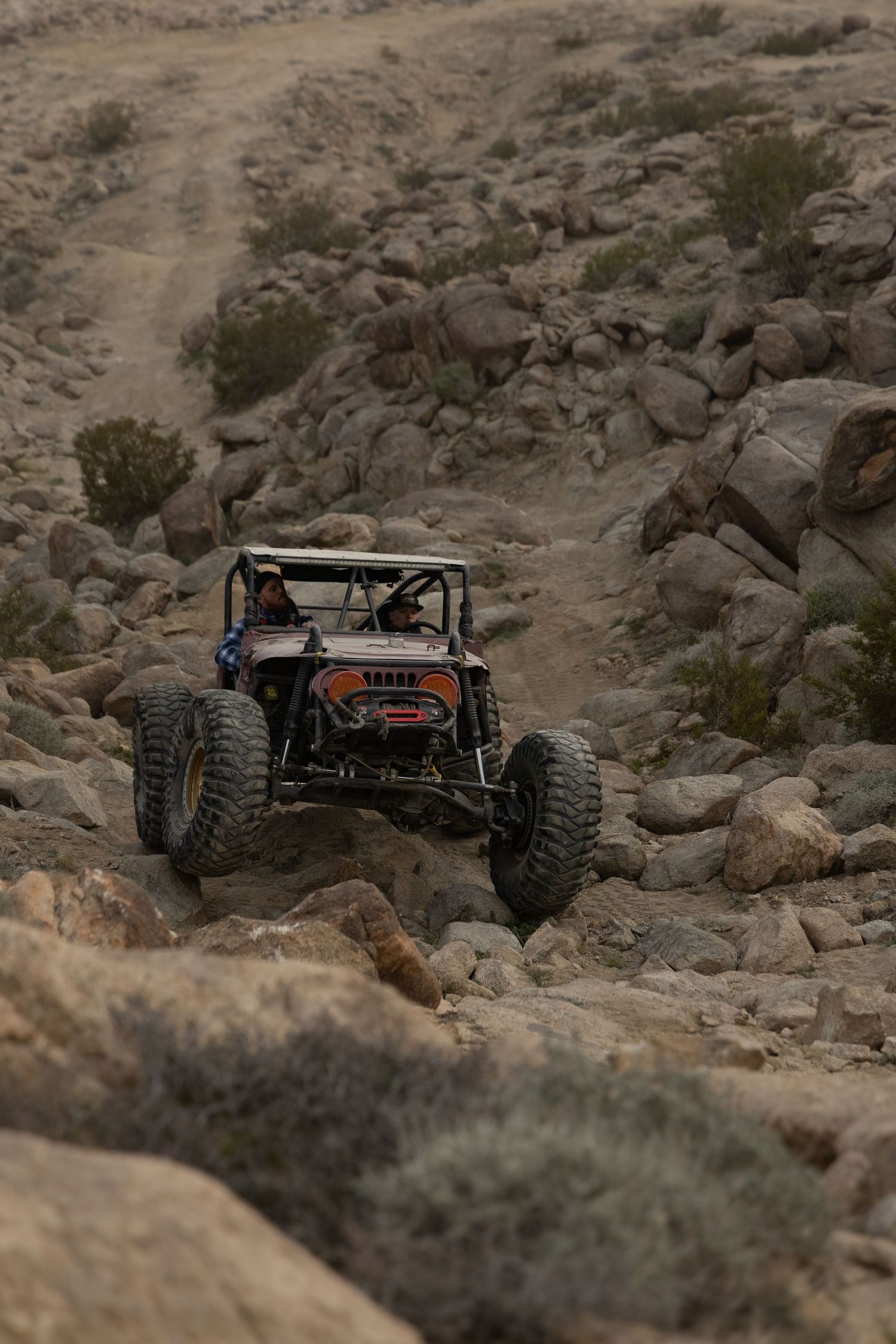 Off-road vehicle navigates rocky desert terrain with large all-terrain tires and custom suspension setup.