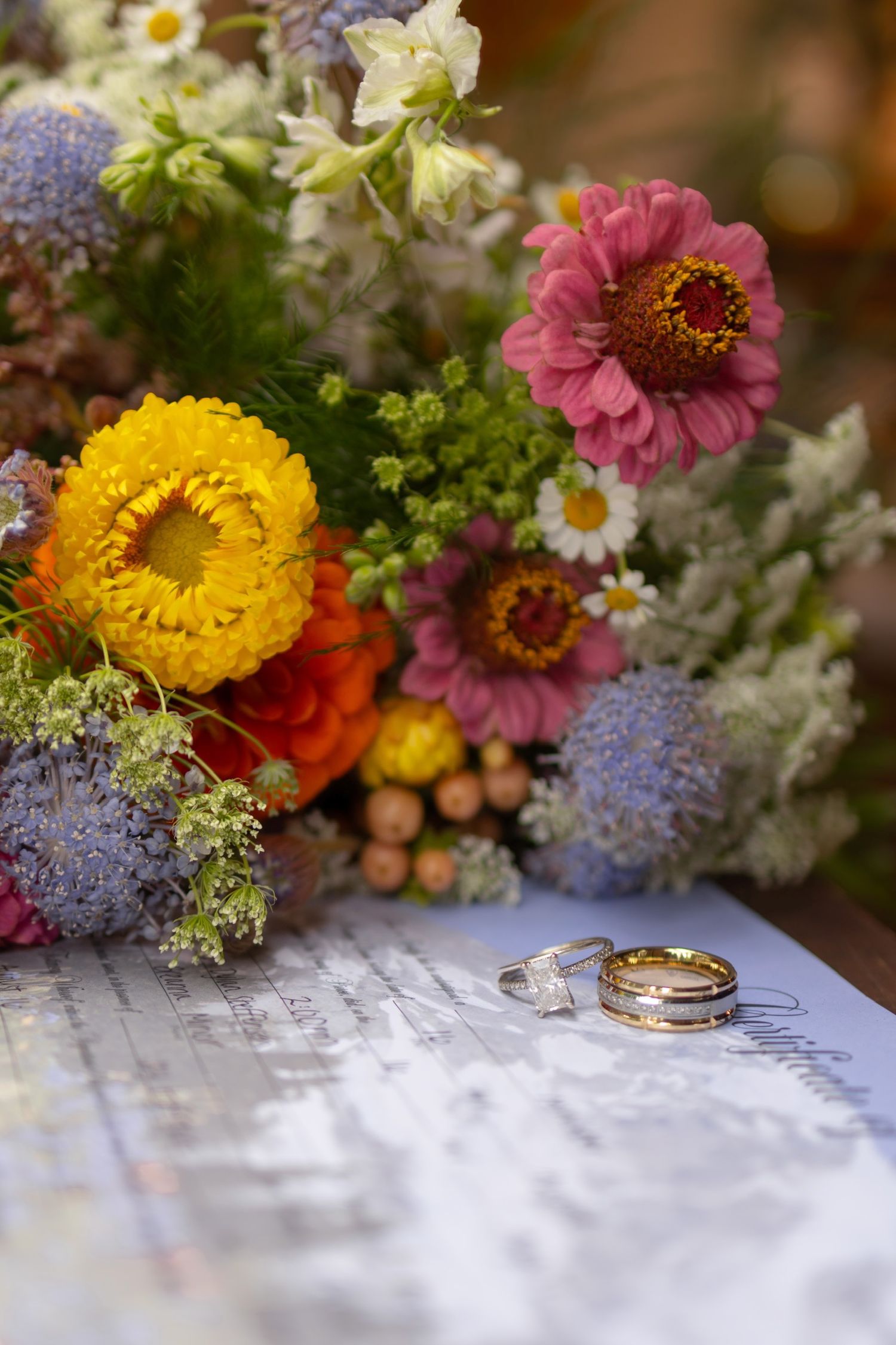 Colorful wildflower bouquet with wedding rings on white surface.