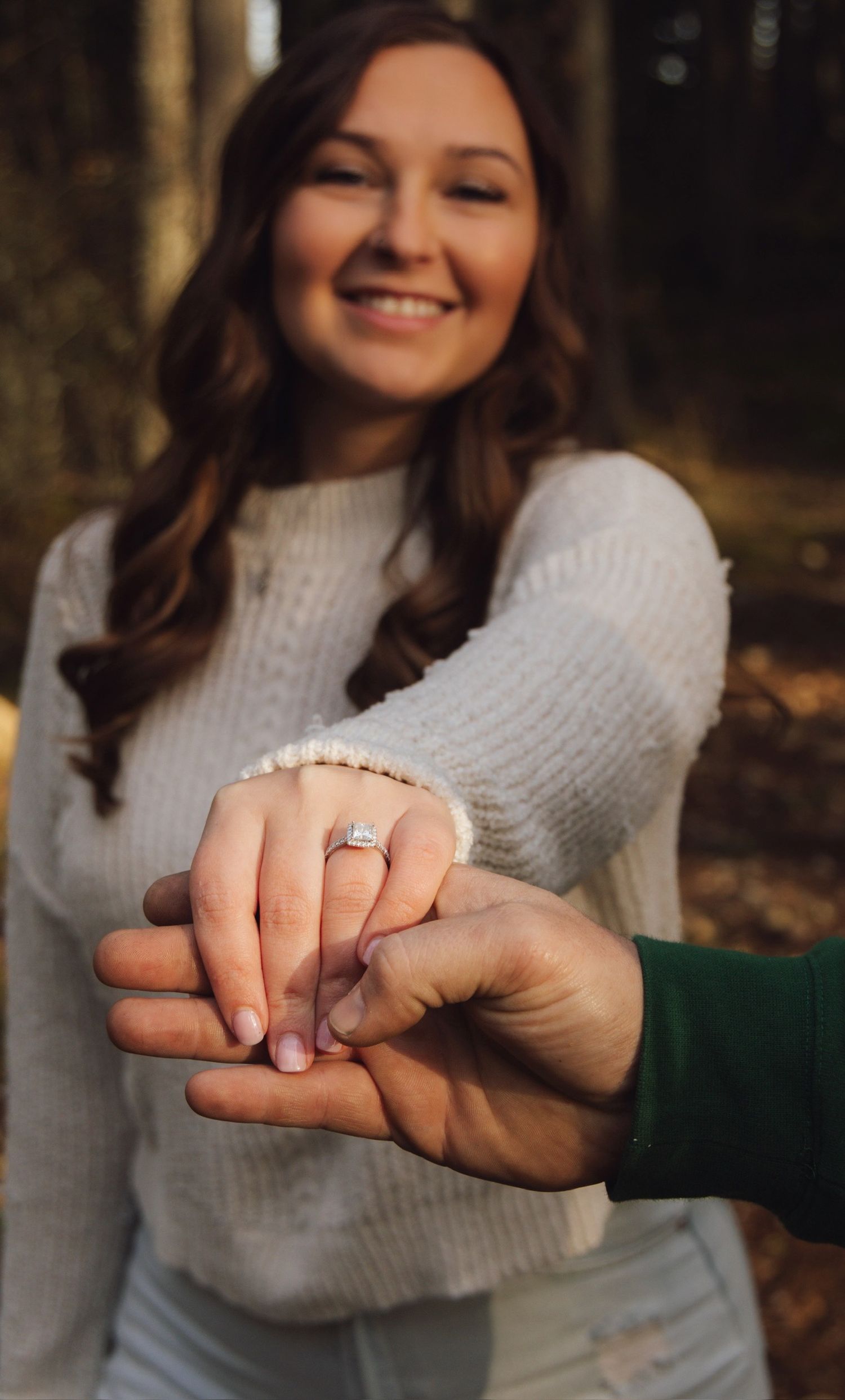 Close-up shot of hands displaying a new engagement ring outdoors.