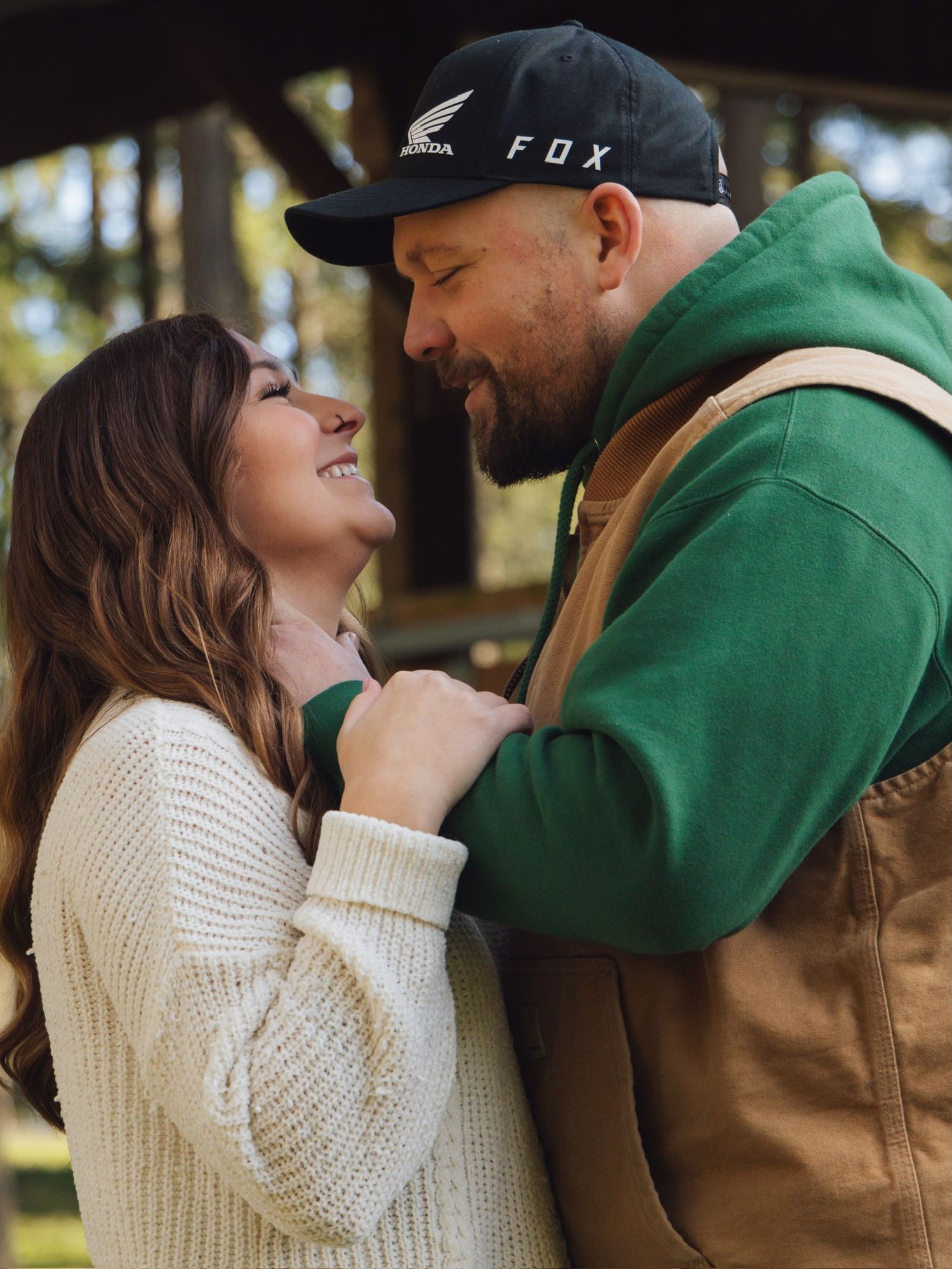 A couple sharing a joyful moment outdoors, wearing casual winter attire including a Fox hat and green hoodie.