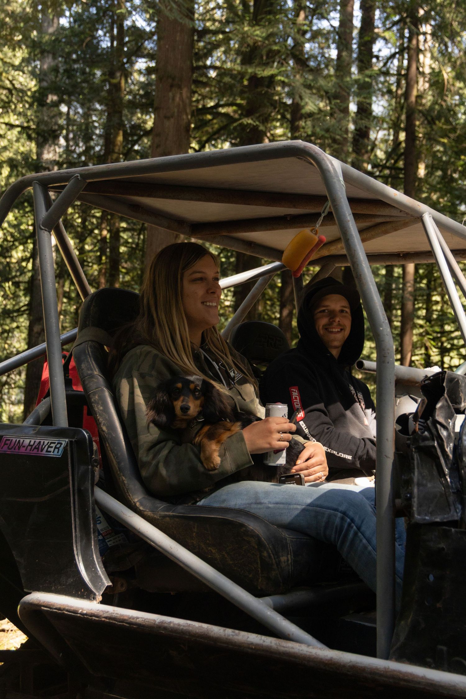 A group of friends laugh and smile while sitting in a recreational vehicle in a forested area.
