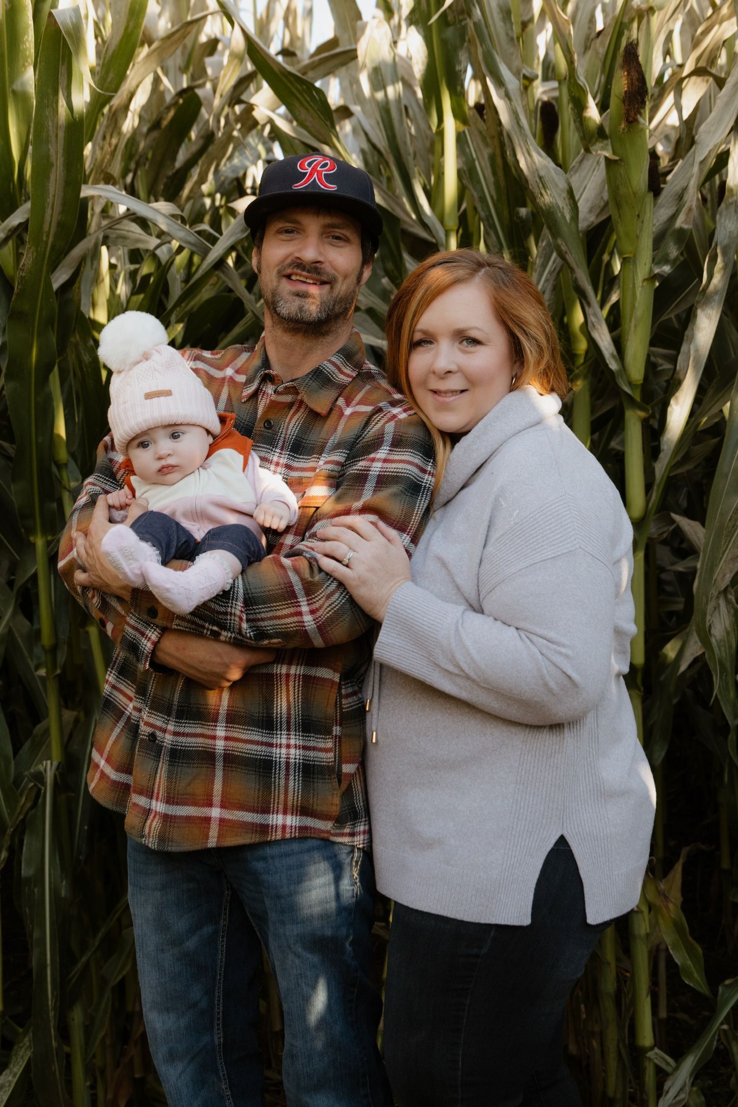 Family poses together in front of tall corn stalks during an autumn photo session.