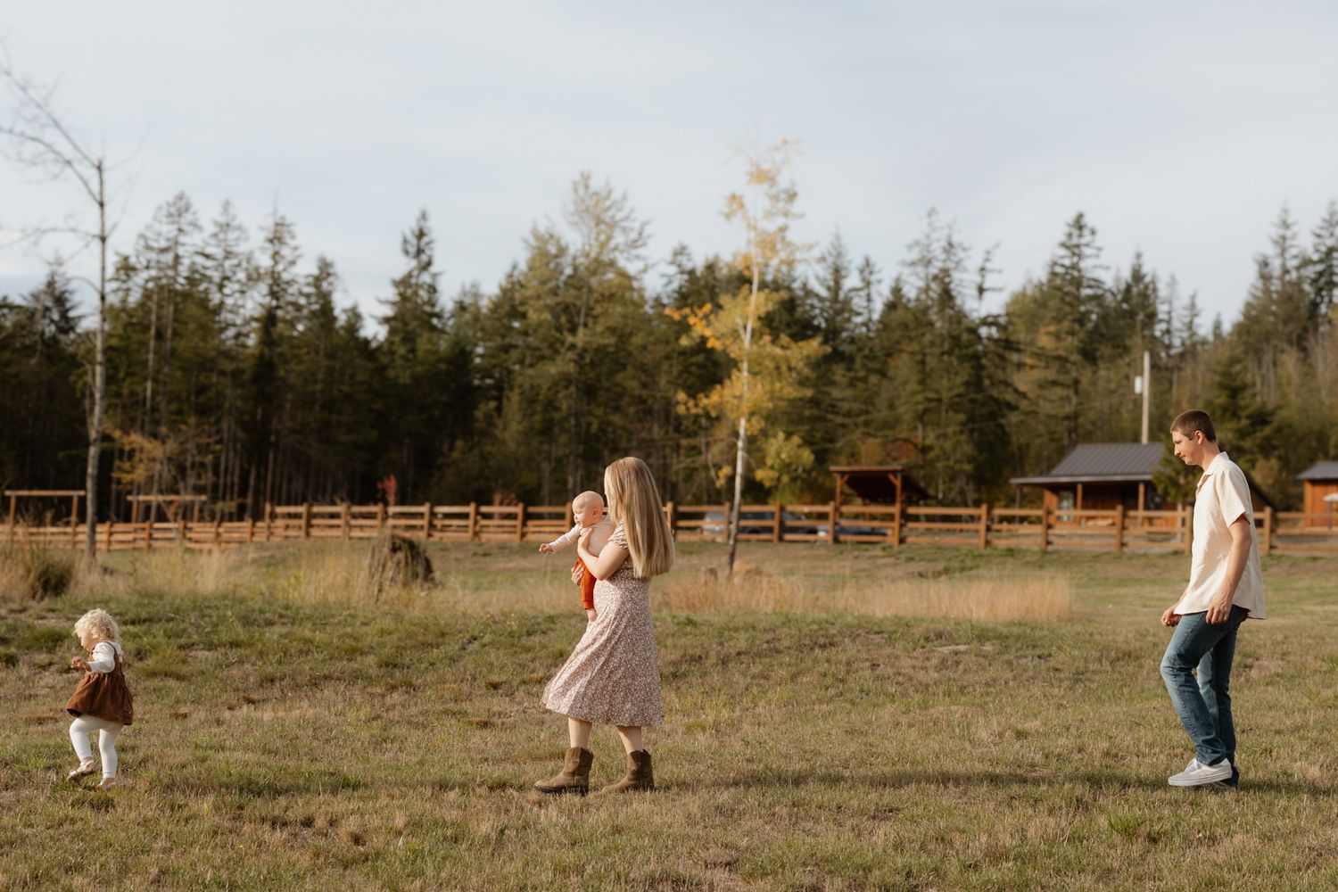 Three people playing together in an open field with a wooden fence and forest in the background.