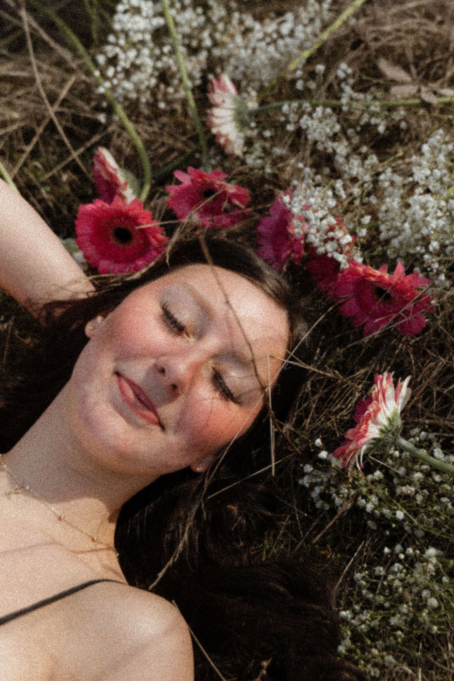 A dreamy portrait of someone lying in grass surrounded by pink gerbera daisies and delicate white baby's breath flowers.