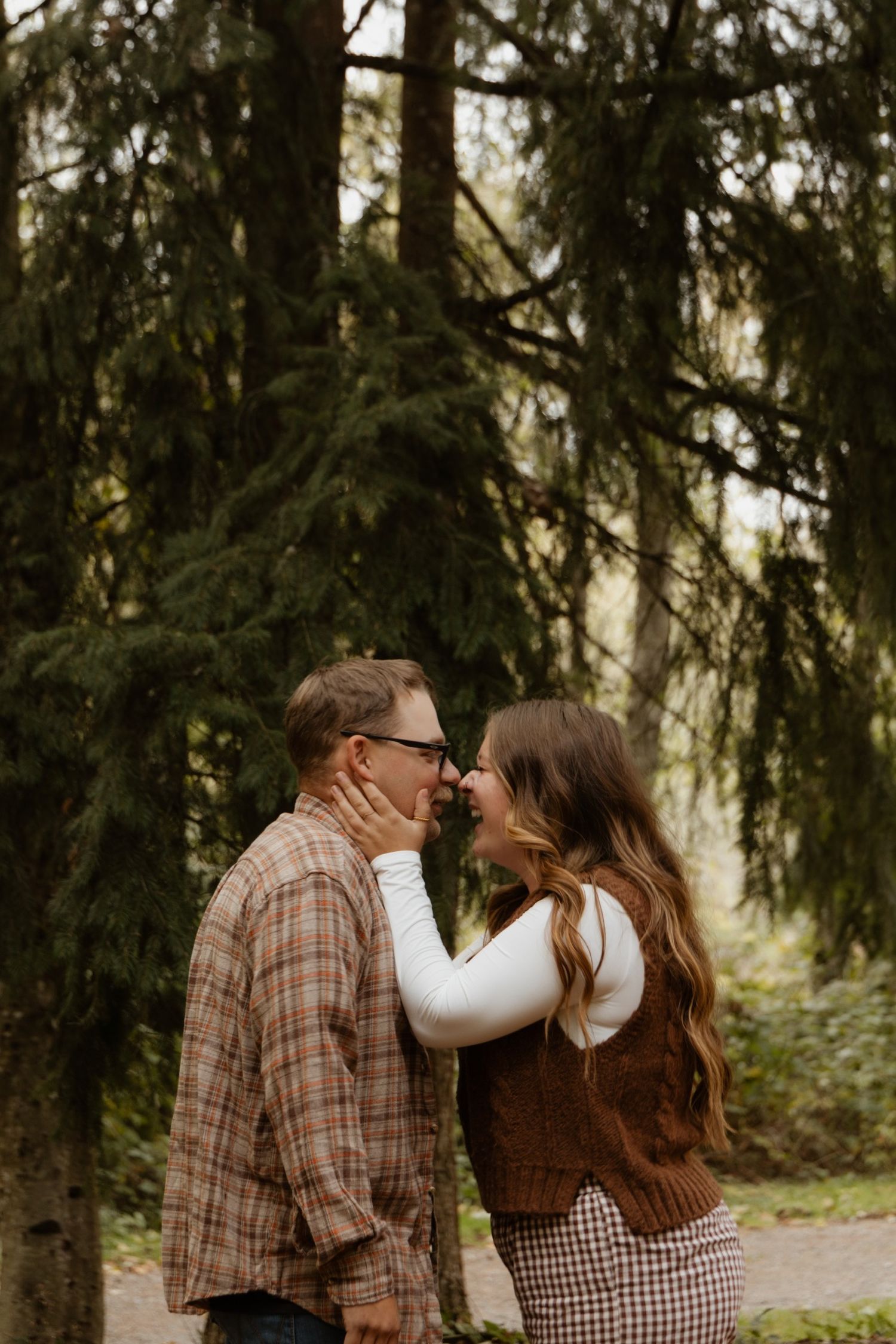 Romantic couple sharing an intimate moment among evergreen trees.