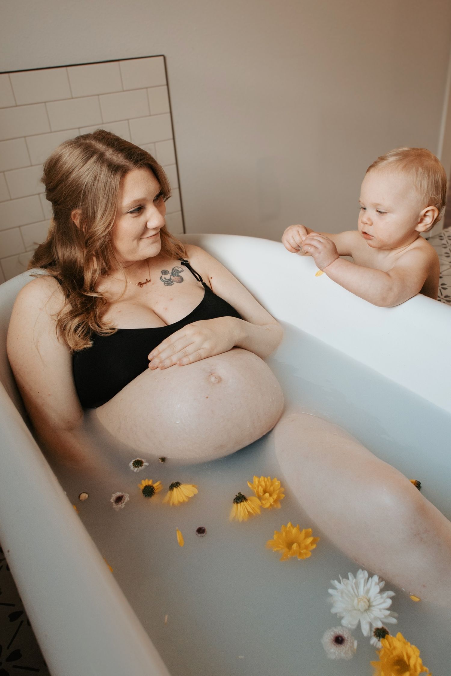 A serene milk bath maternity photoshoot features floating flowers and a gentle touch in a white bathtub.