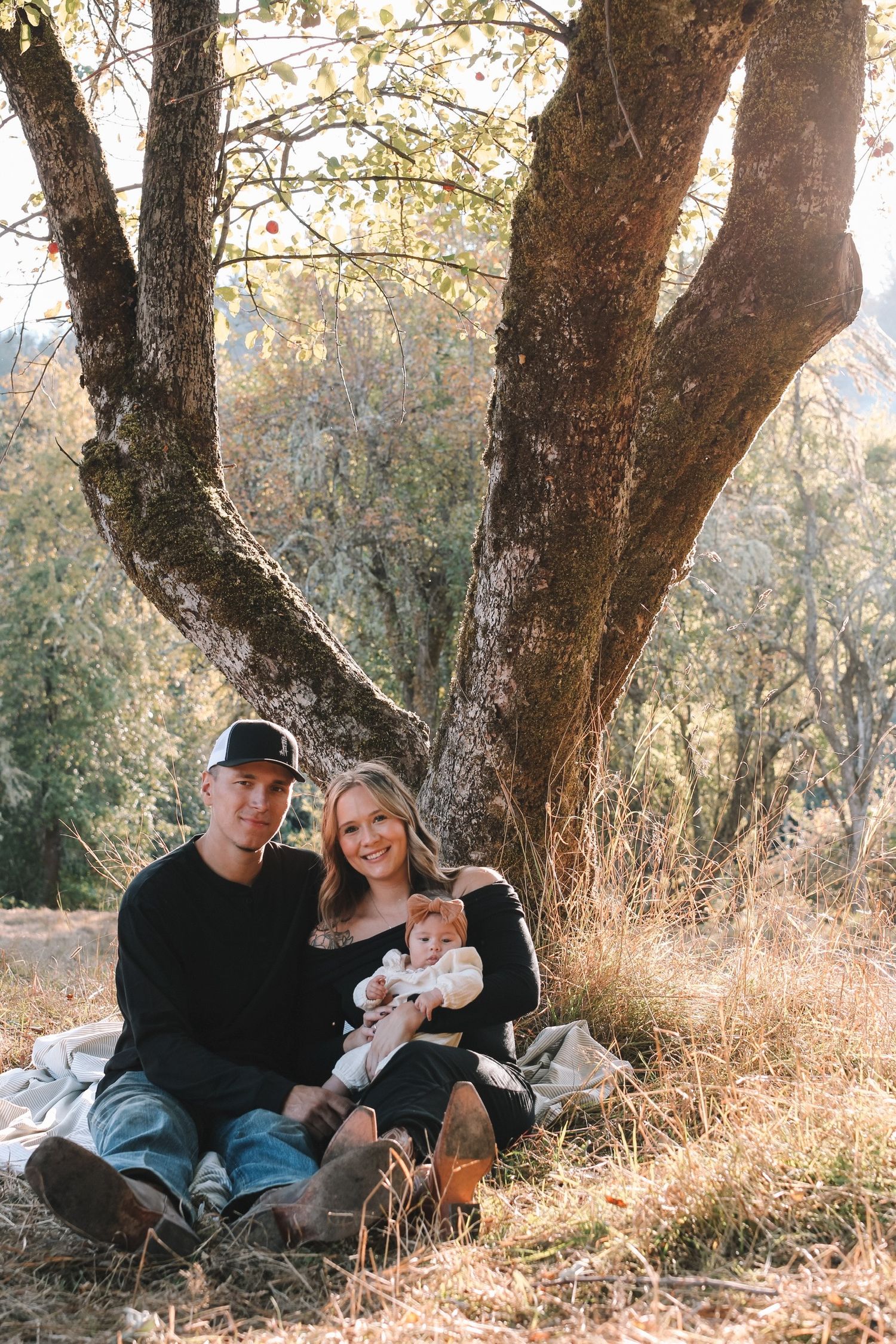 Couple relaxing under large oak trees in autumn sunlight.