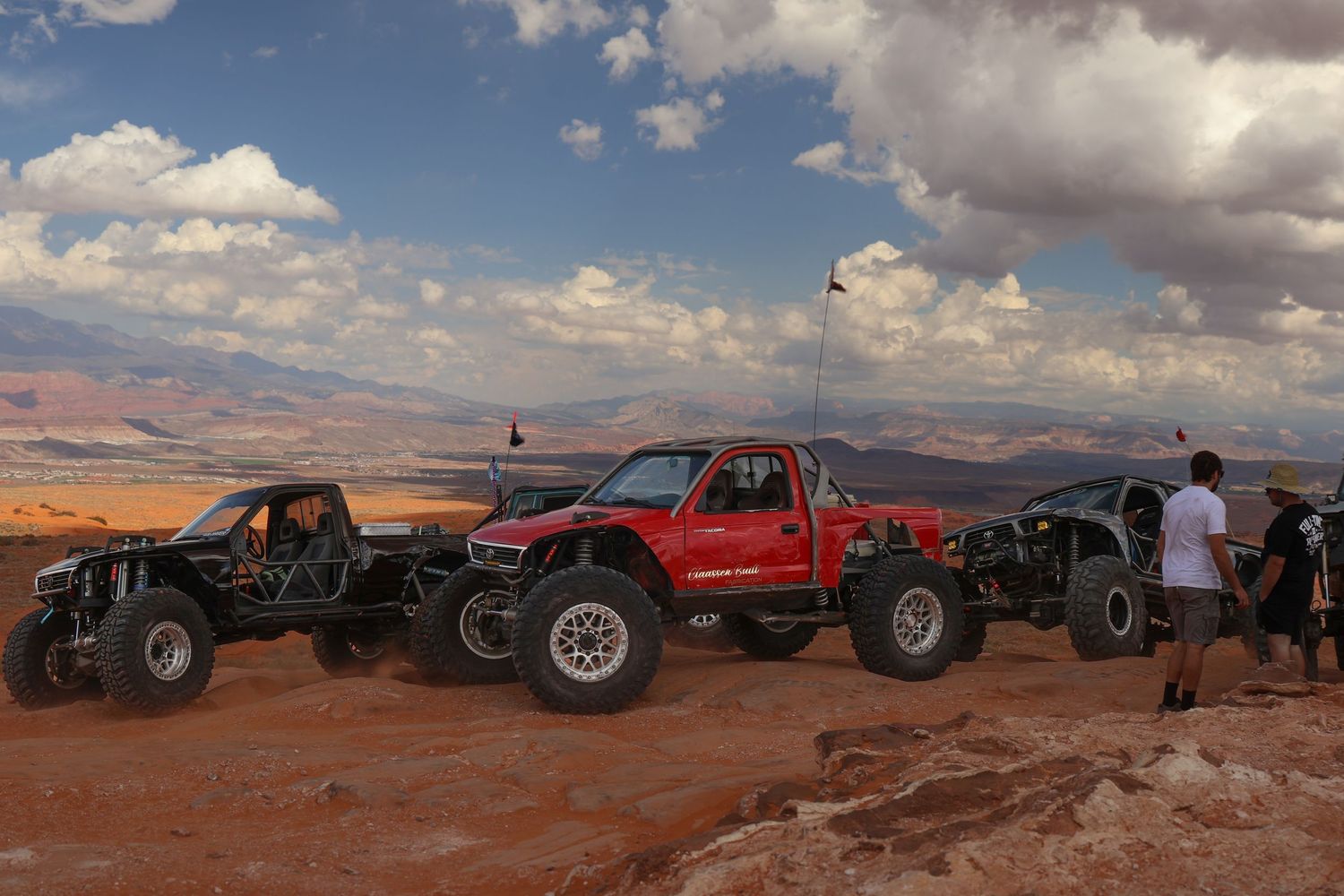 Off-road vehicles lined up against a scenic desert landscape with red rock formations and cloudy skies in the background.