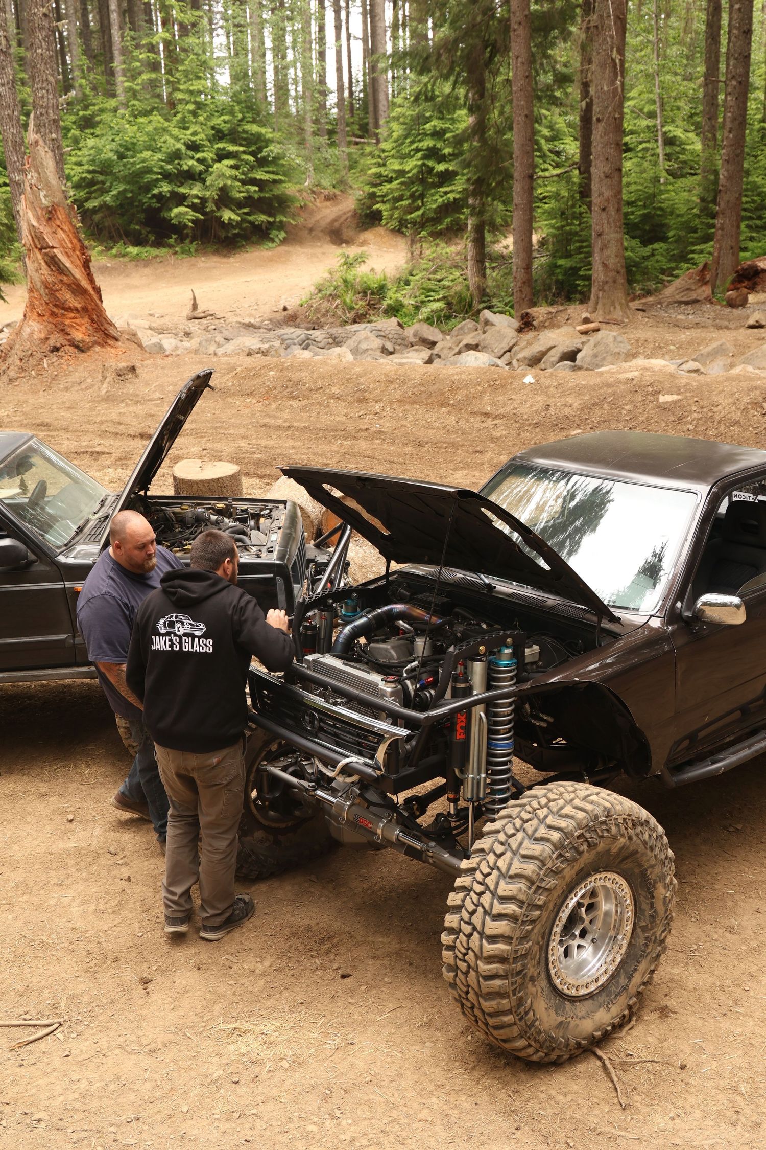 A sequence of four images showing someone working on a black off-road vehicle with large tires in a wooded area.