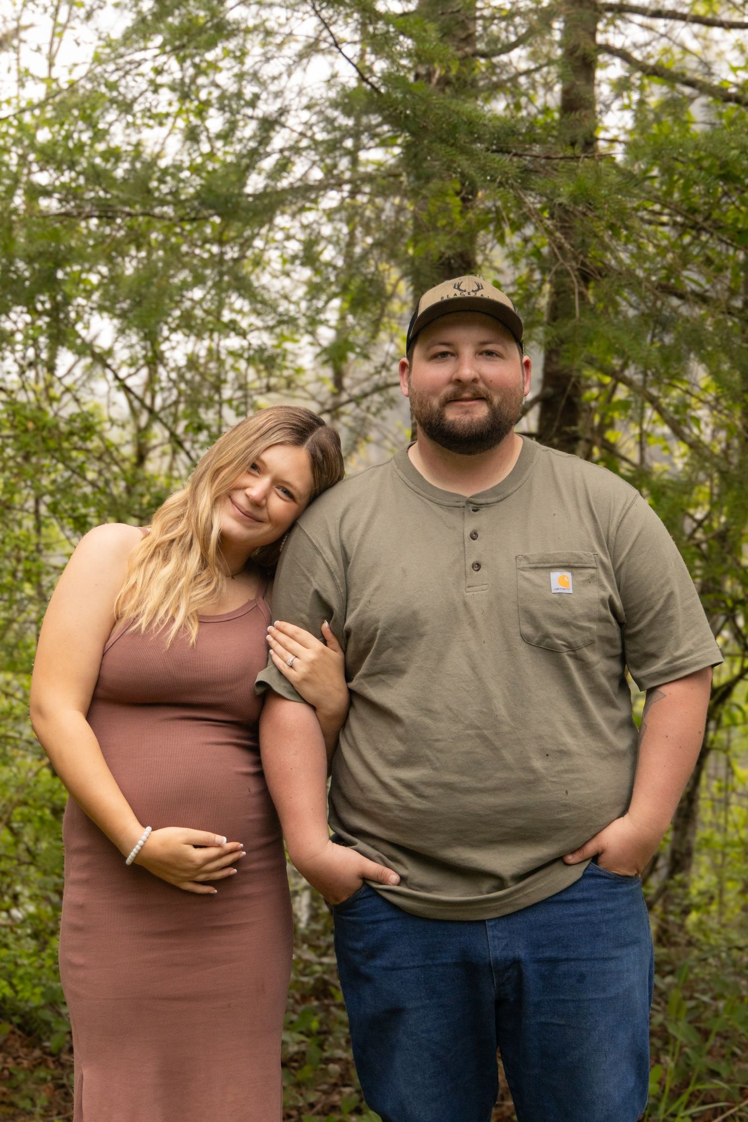 Couple embracing during outdoor maternity photo shoot in nature.
