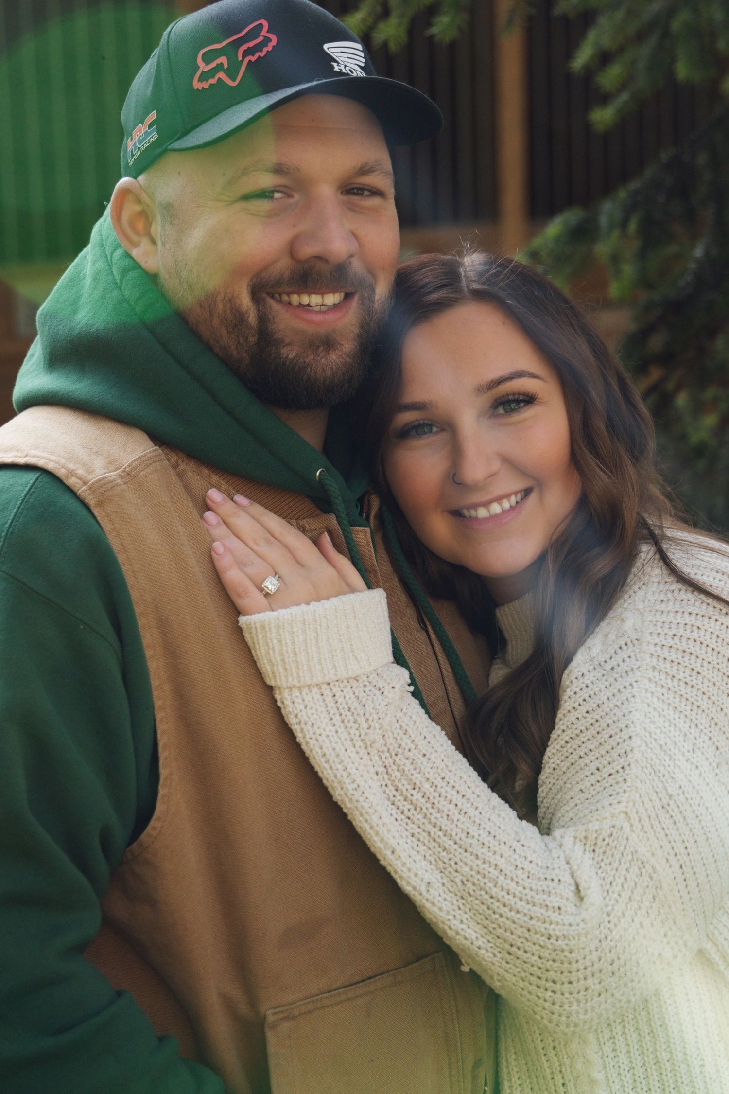 Couple in casual outdoor wear sharing intimate moment against green background.
