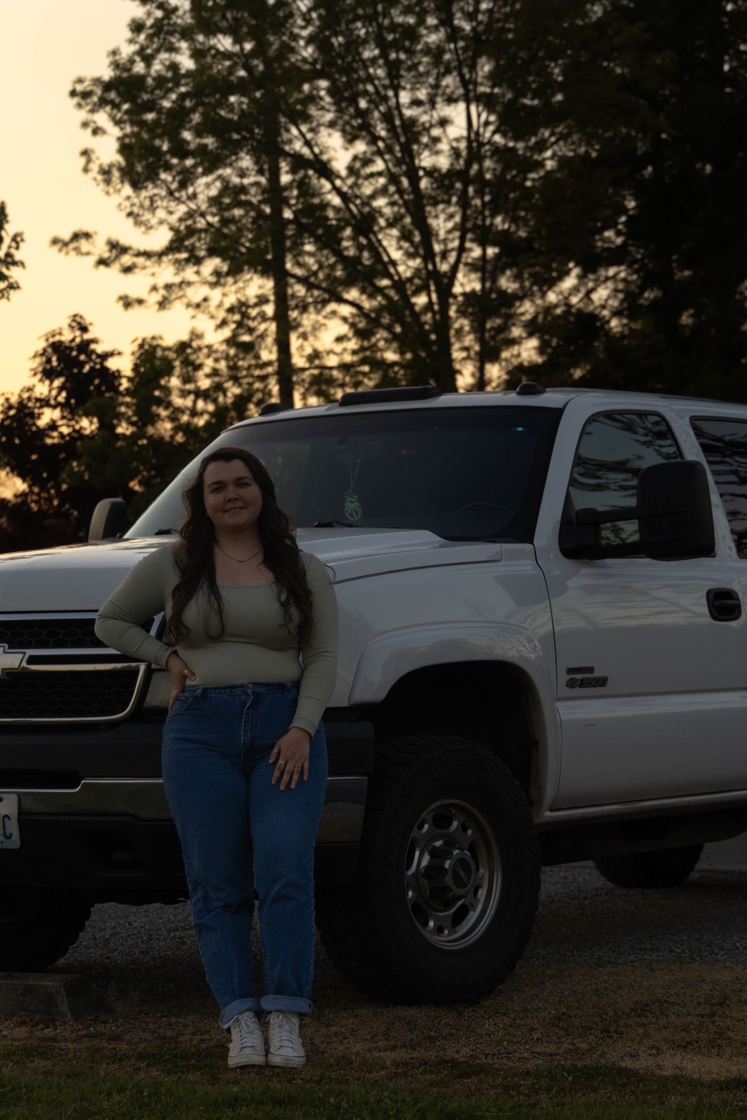 Person in casual attire poses next to white pickup truck at dusk.