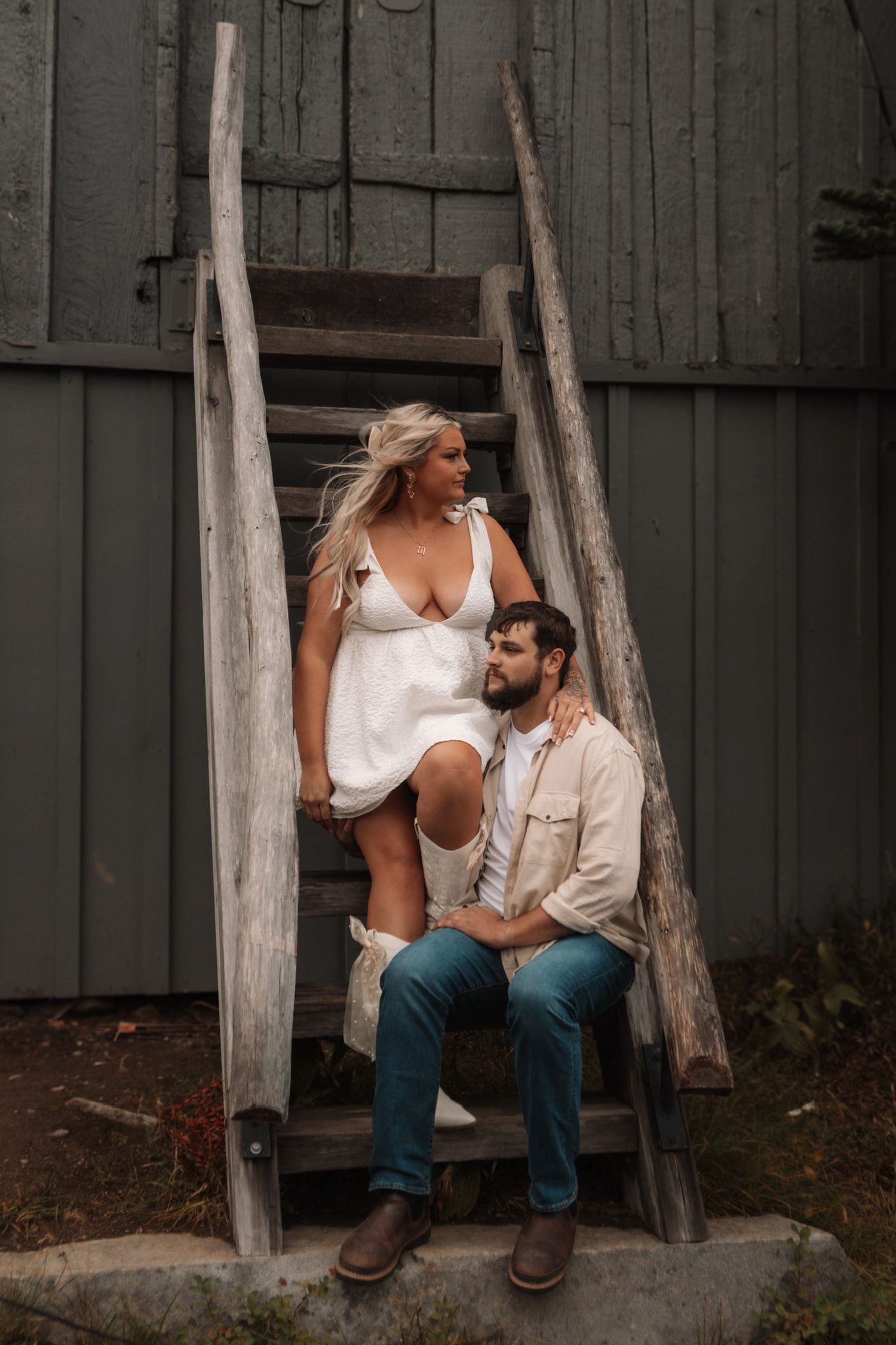 A couple sits close together on wooden steps against a rustic backdrop.