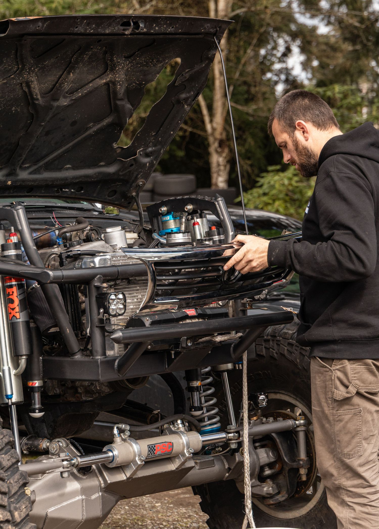 Mechanic working under raised vehicle chassis in repair shop setting.