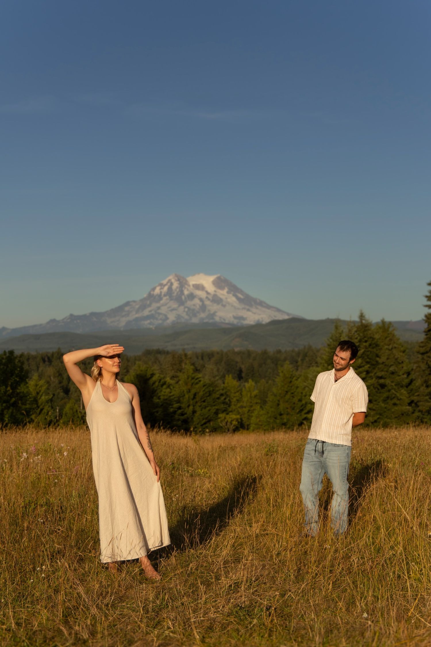 People pose in a field with Mount Rainier visible in the background during sunset.