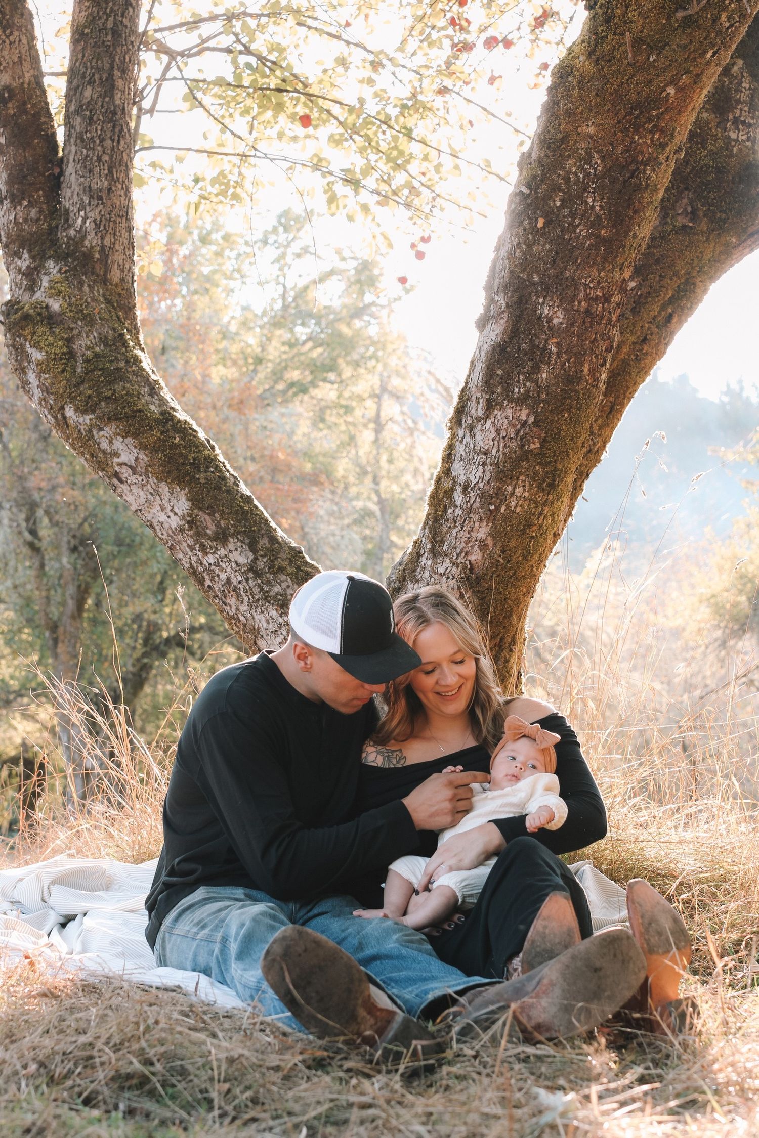 A family shares tender moments together while relaxing under a tree in an autumn woodland setting.