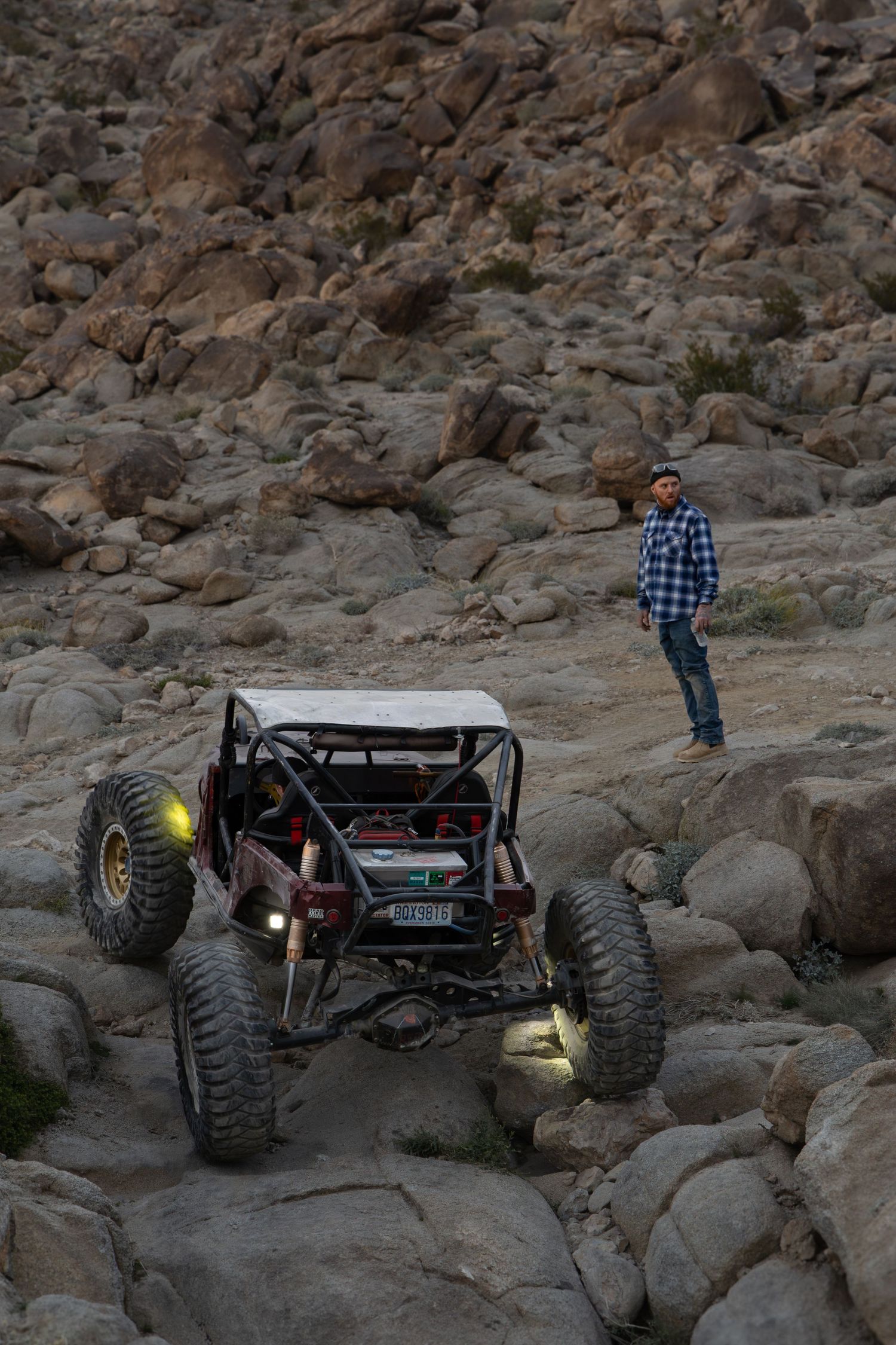 Off-road vehicle navigates challenging rocky terrain on a rugged mountain trail with large boulders and steep inclines.