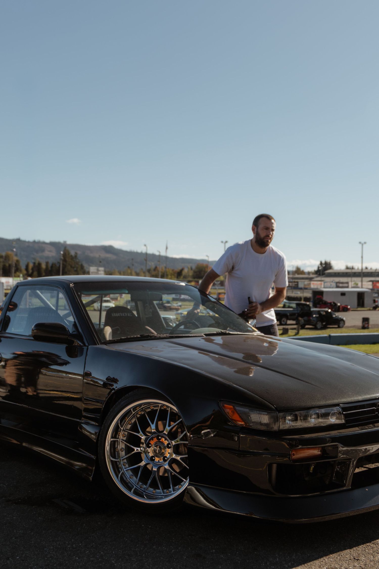 Black sports car with custom chrome wheels parked at a car meet during sunset with mountains in background.