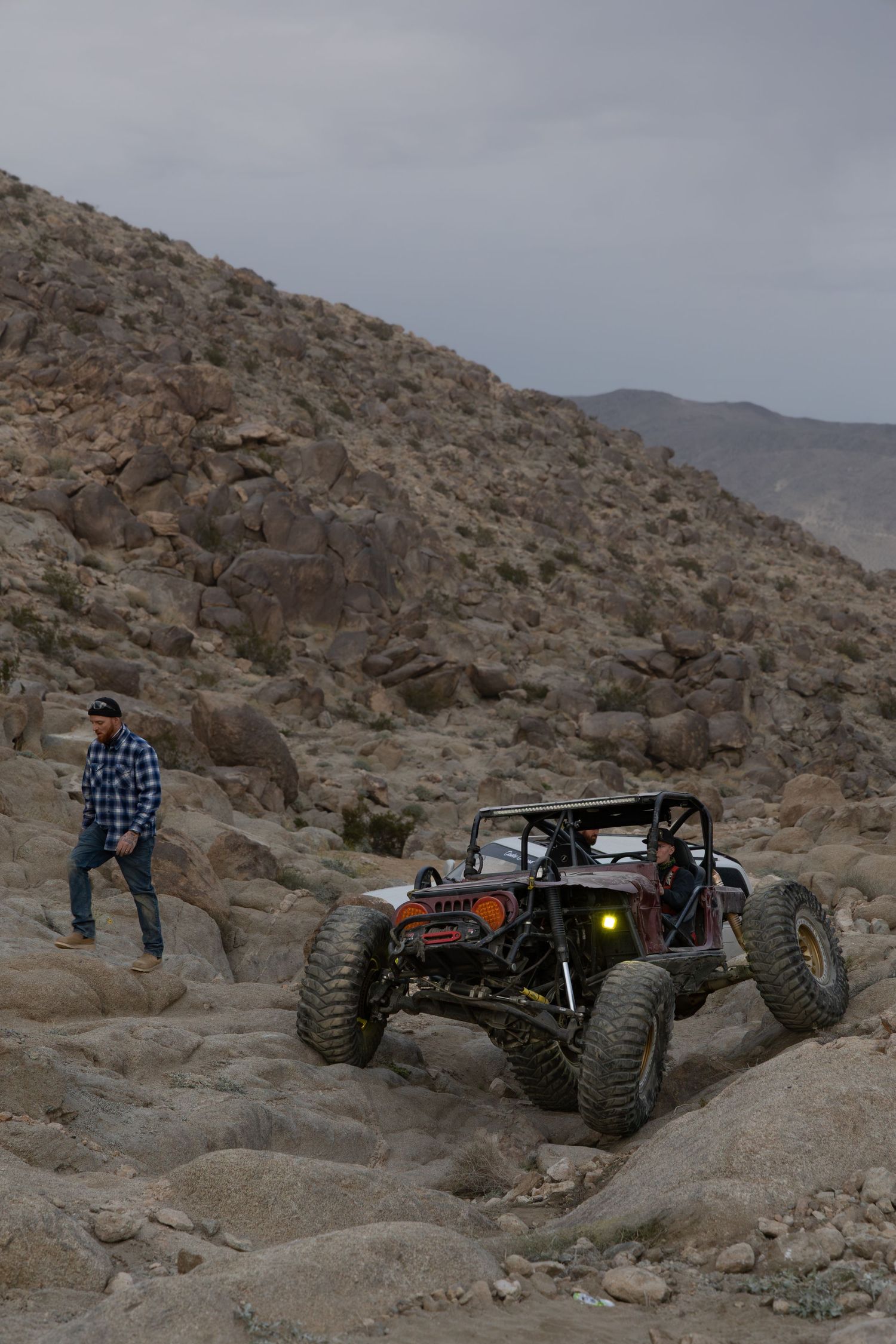 Off-road vehicle navigates challenging rocky terrain on a mountainous desert trail while being photographed in sequence.