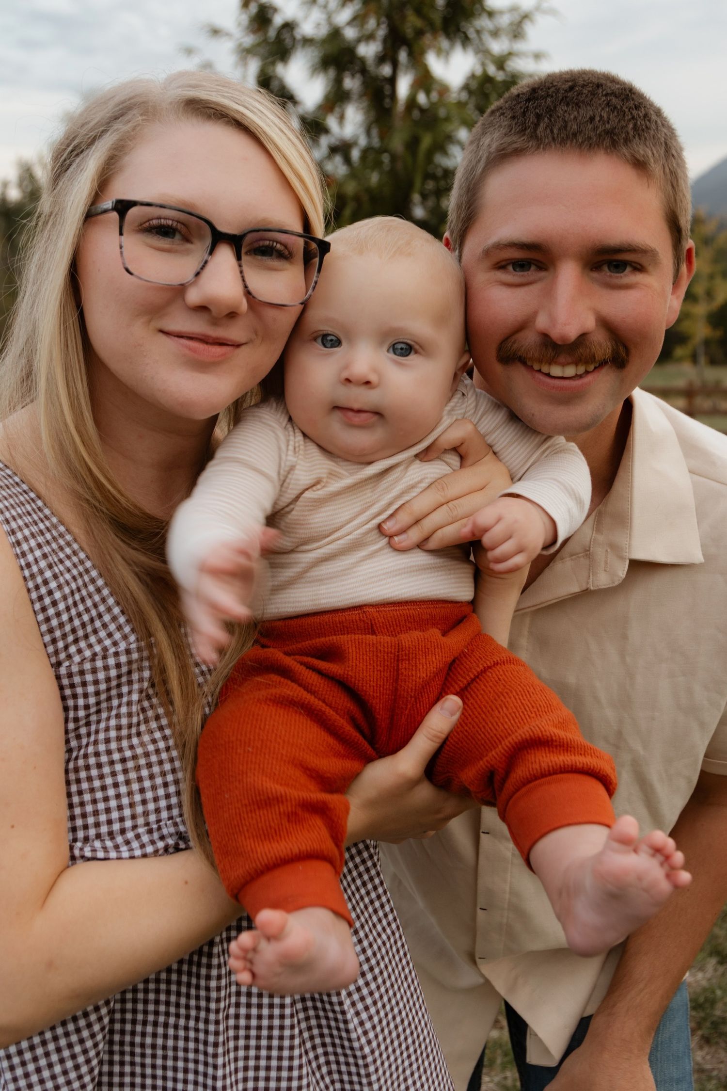 A sweet family portrait taken outdoors against a backdrop of evergreen trees.