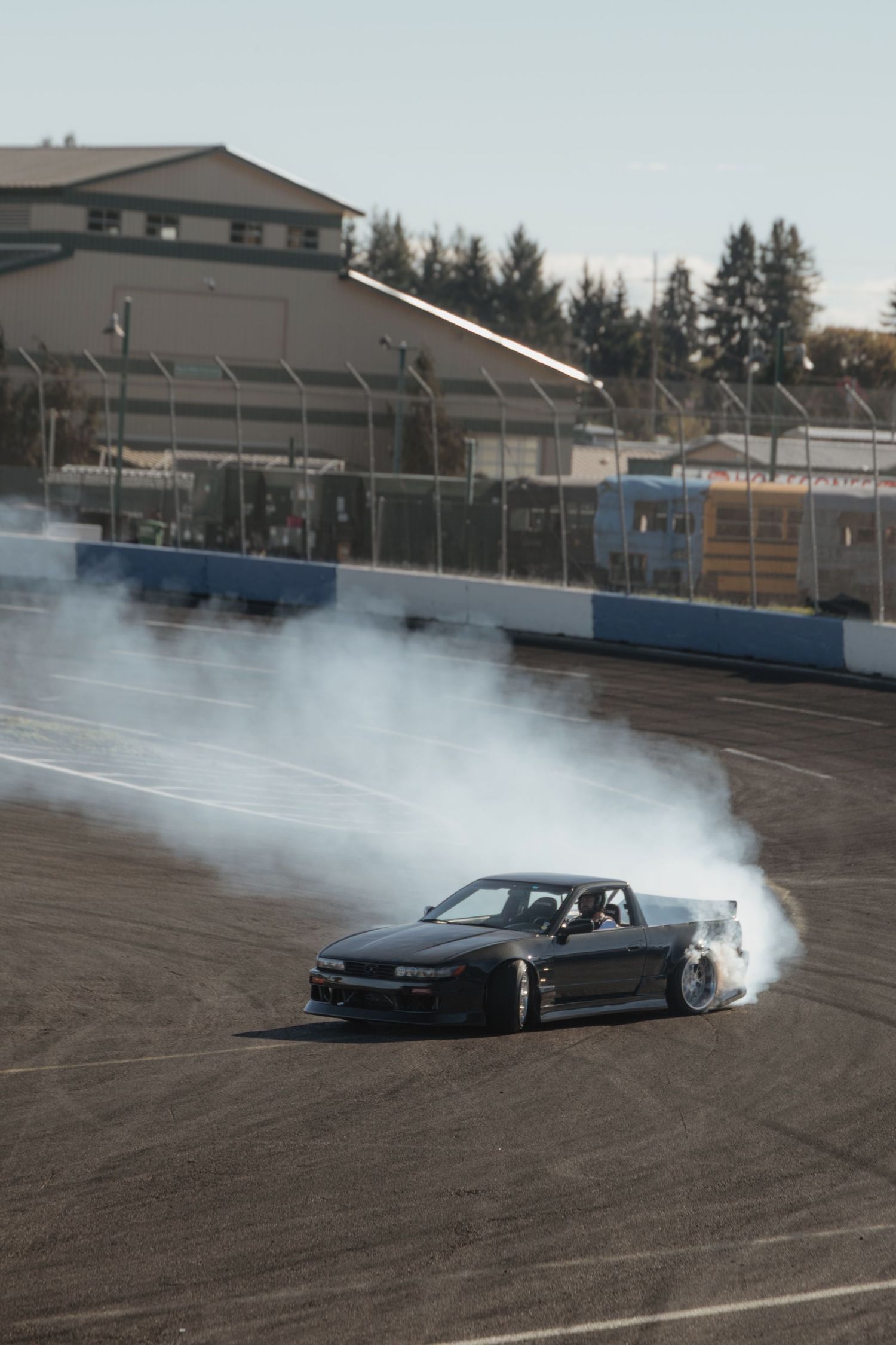 A black sports car performing a drift with smoke trails on a race track.