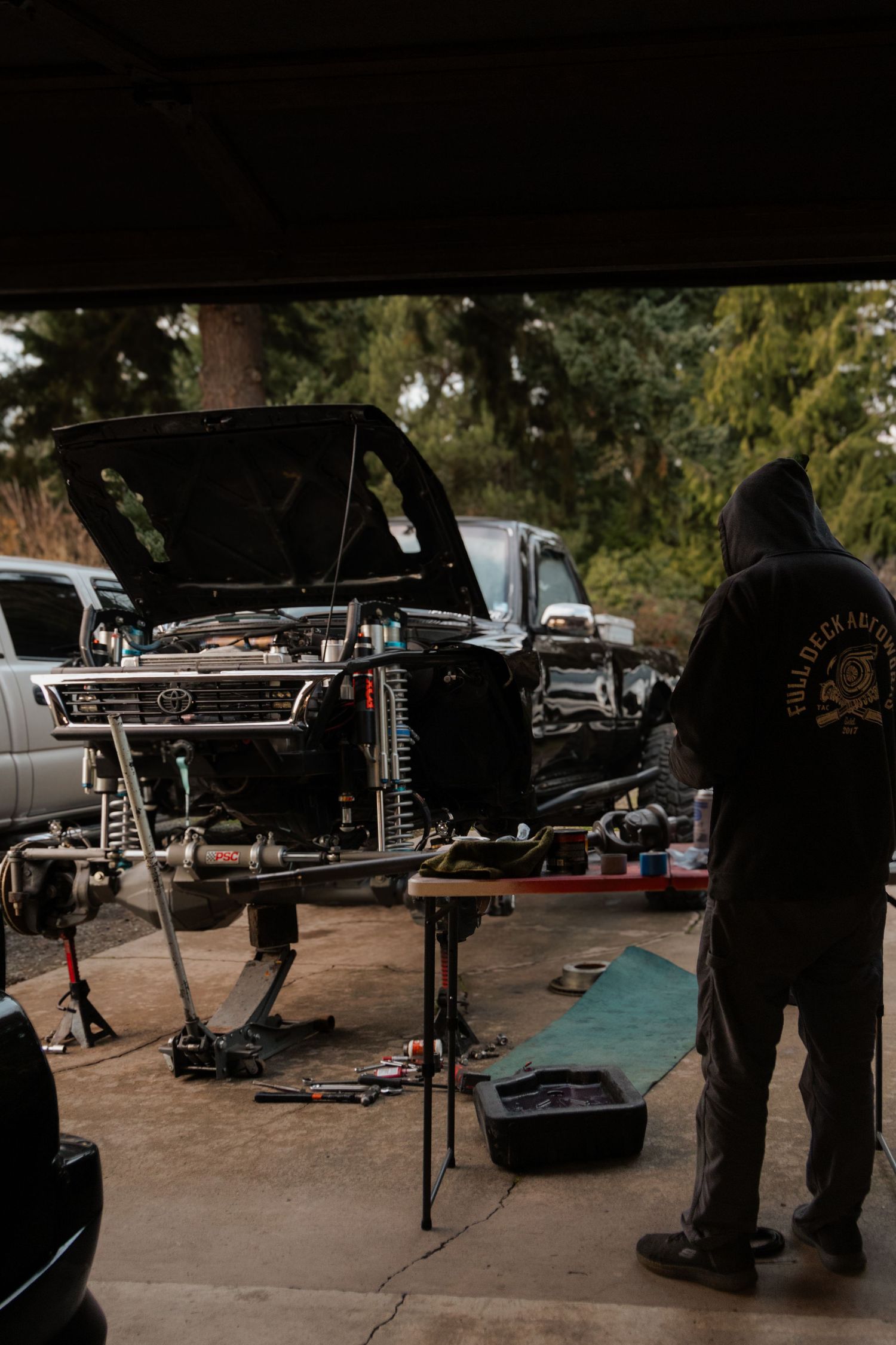 Auto repair shop workspace with multiple vehicles and tools visible in dimly lit area.