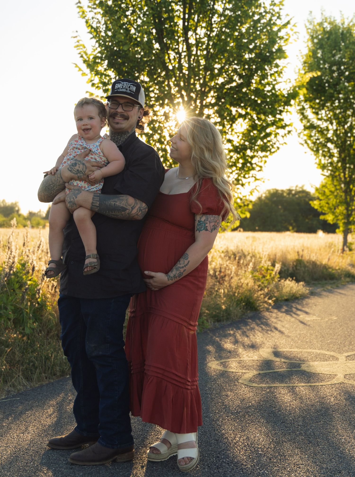 A family shares a tender moment together at sunset on a gravel path surrounded by trees and tall grass.