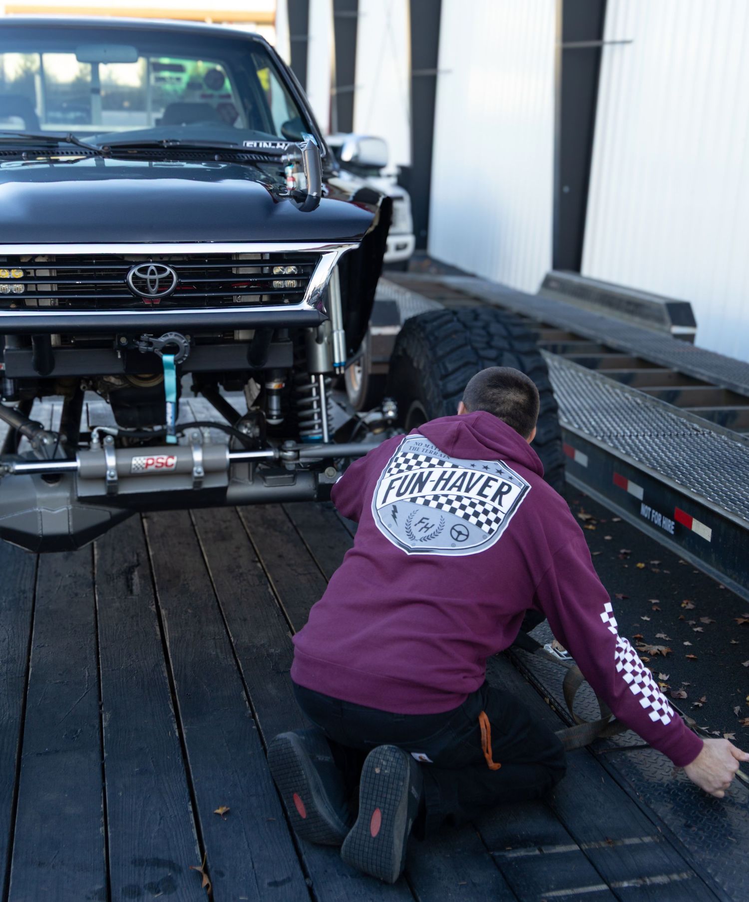 Burgundy hooded sweatshirt with racing designs shown on wooden deck near vehicles.