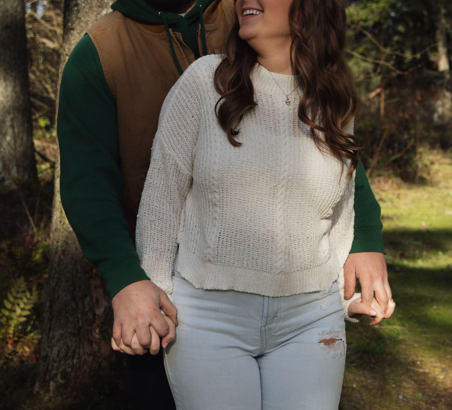Close-up of someone wearing a cream sweater and light-colored jeans in an outdoor setting.