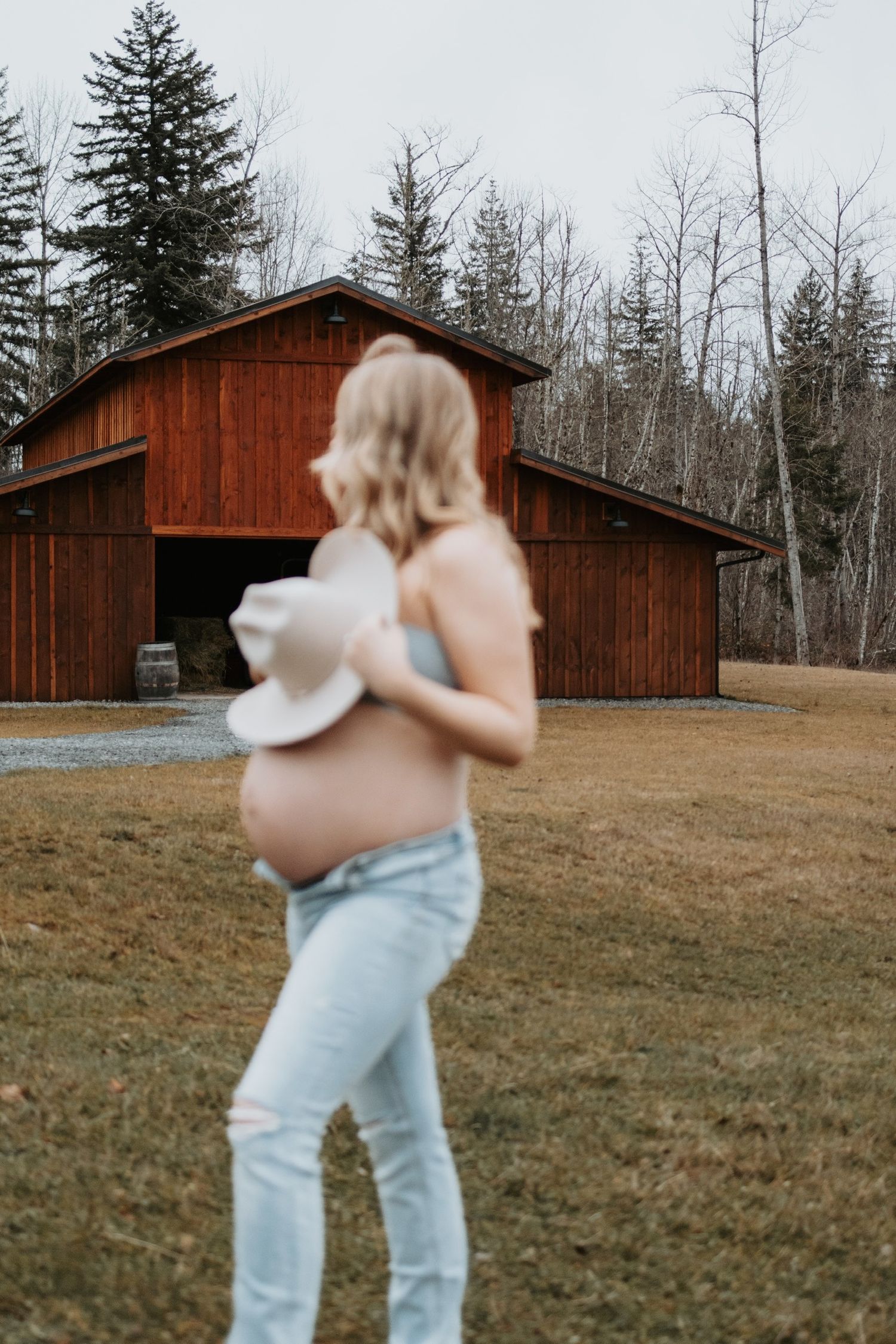 Expectant mother standing in front of a rustic barn in winter.
